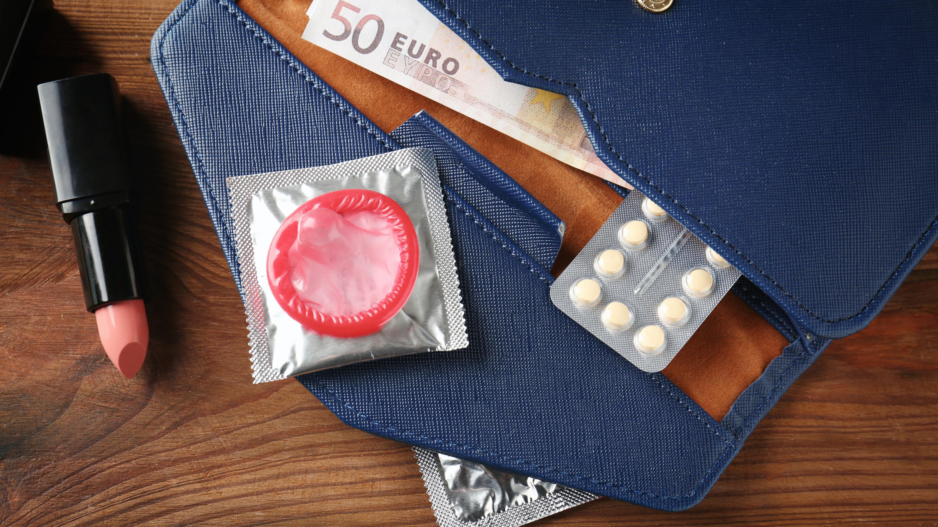 In einer geöffneten Geldbörse sind ein Geldschein, ein Kondom und eine Packung der Pille zu sehen.