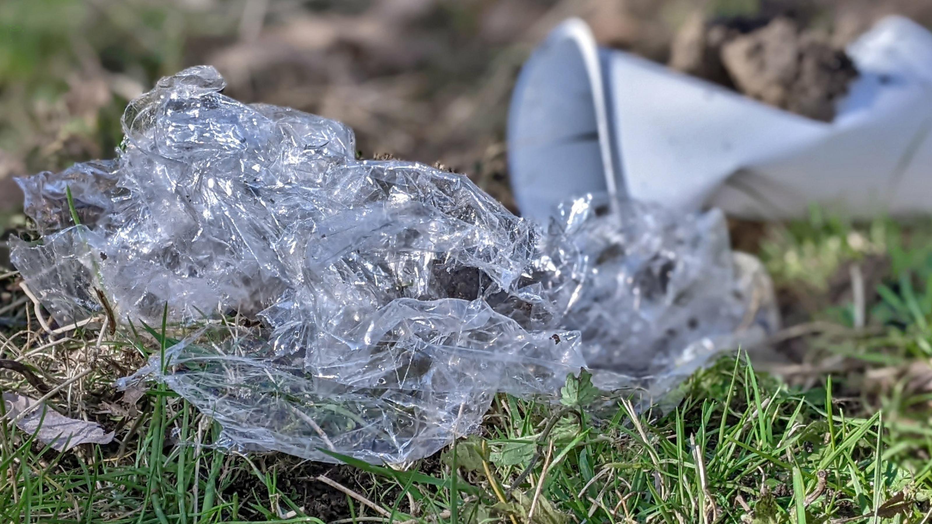 Ein durchsichtige Kunststofffolie und ein weißer Plastikbecher liegen im Gras.