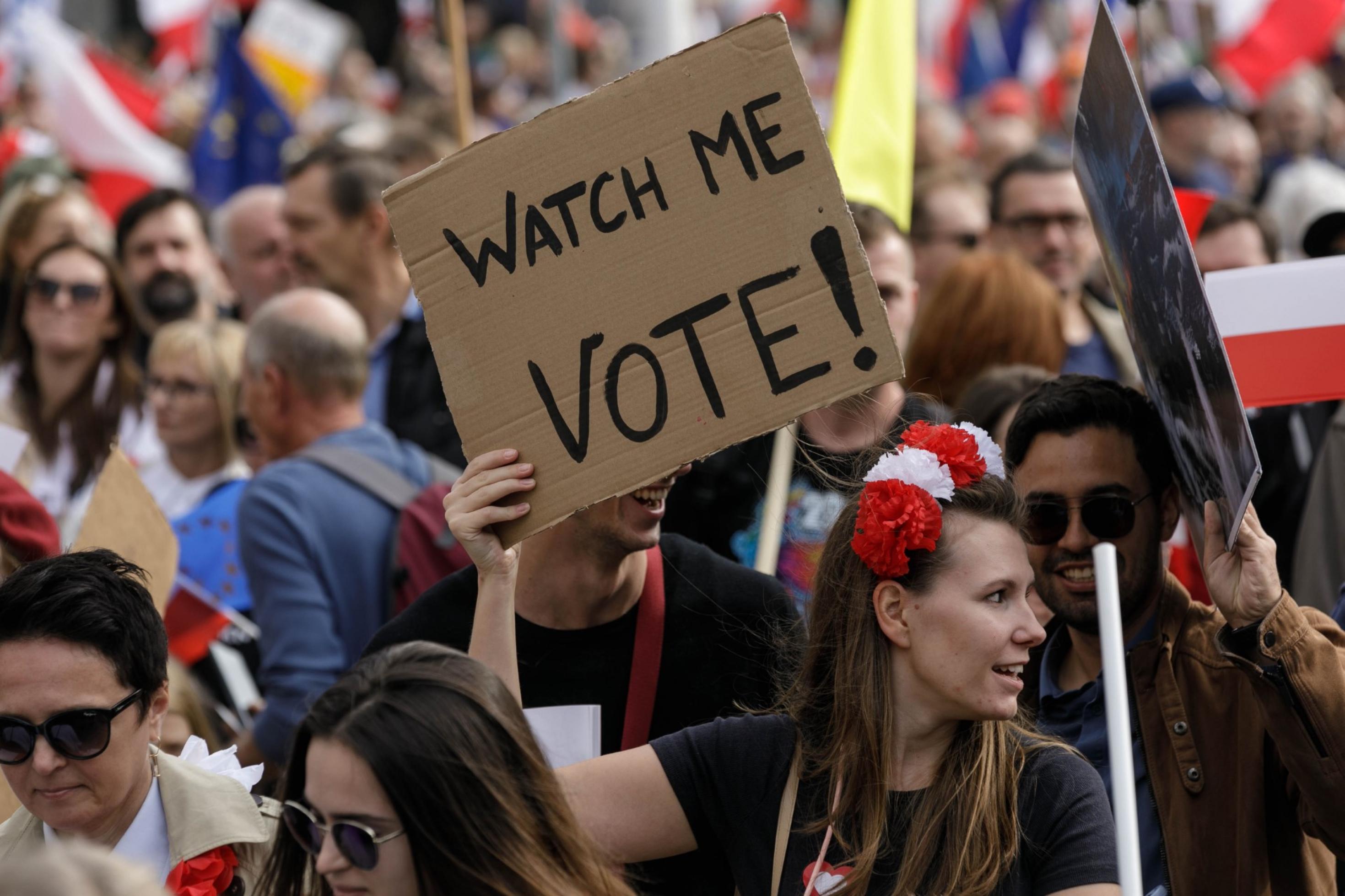 eine Gruppe von Menschen, die Schilder halten. Eine Frau hält ein Schild mit dem Spruch „Watch me Vote“