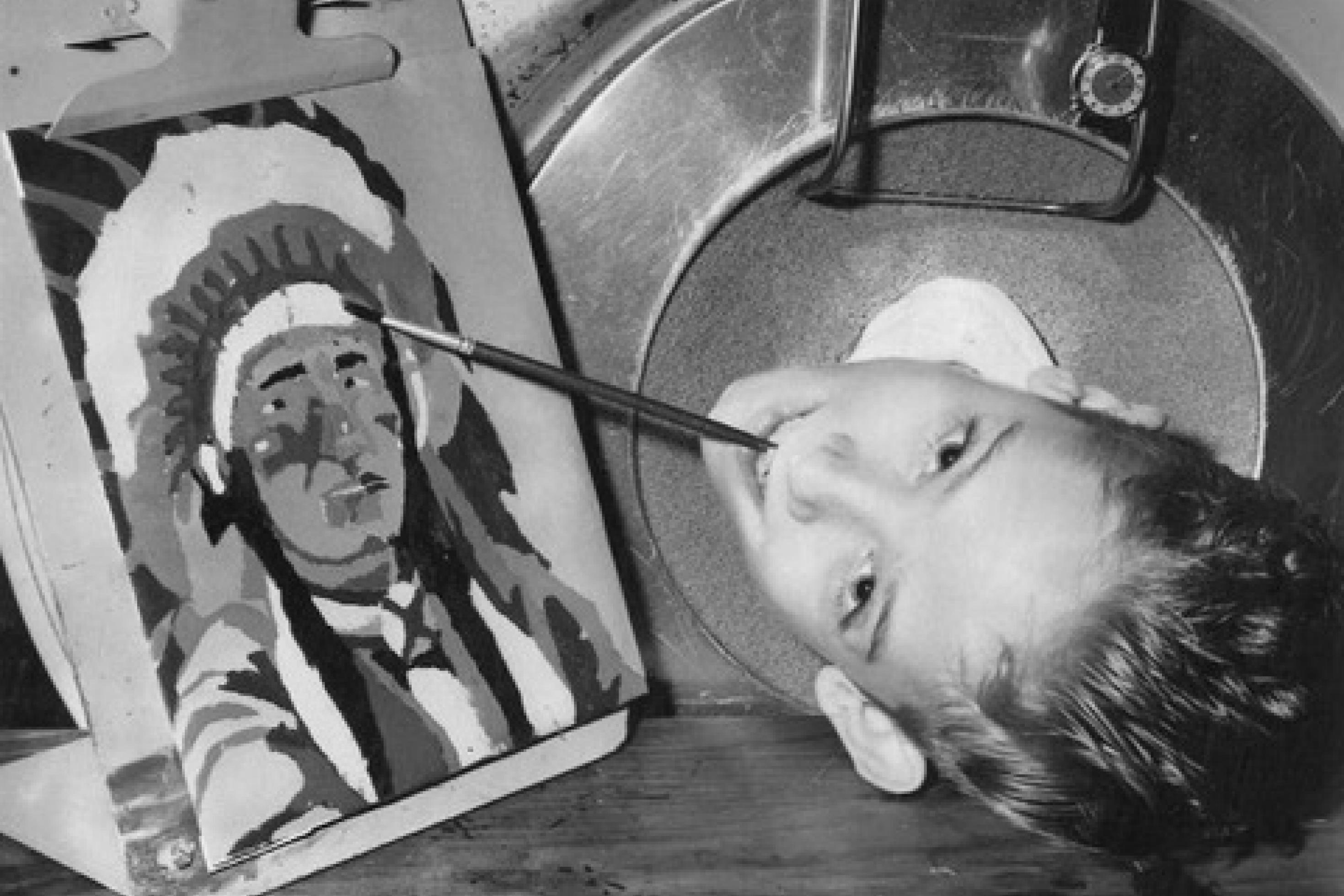 Der Kopf des jungen Paul ragt aus einer Eisernen Lunge. Er hat einen Pinsel in seinem Mund. Neben seinem Kopf steht ein gemaltes Bild eines Indianers.