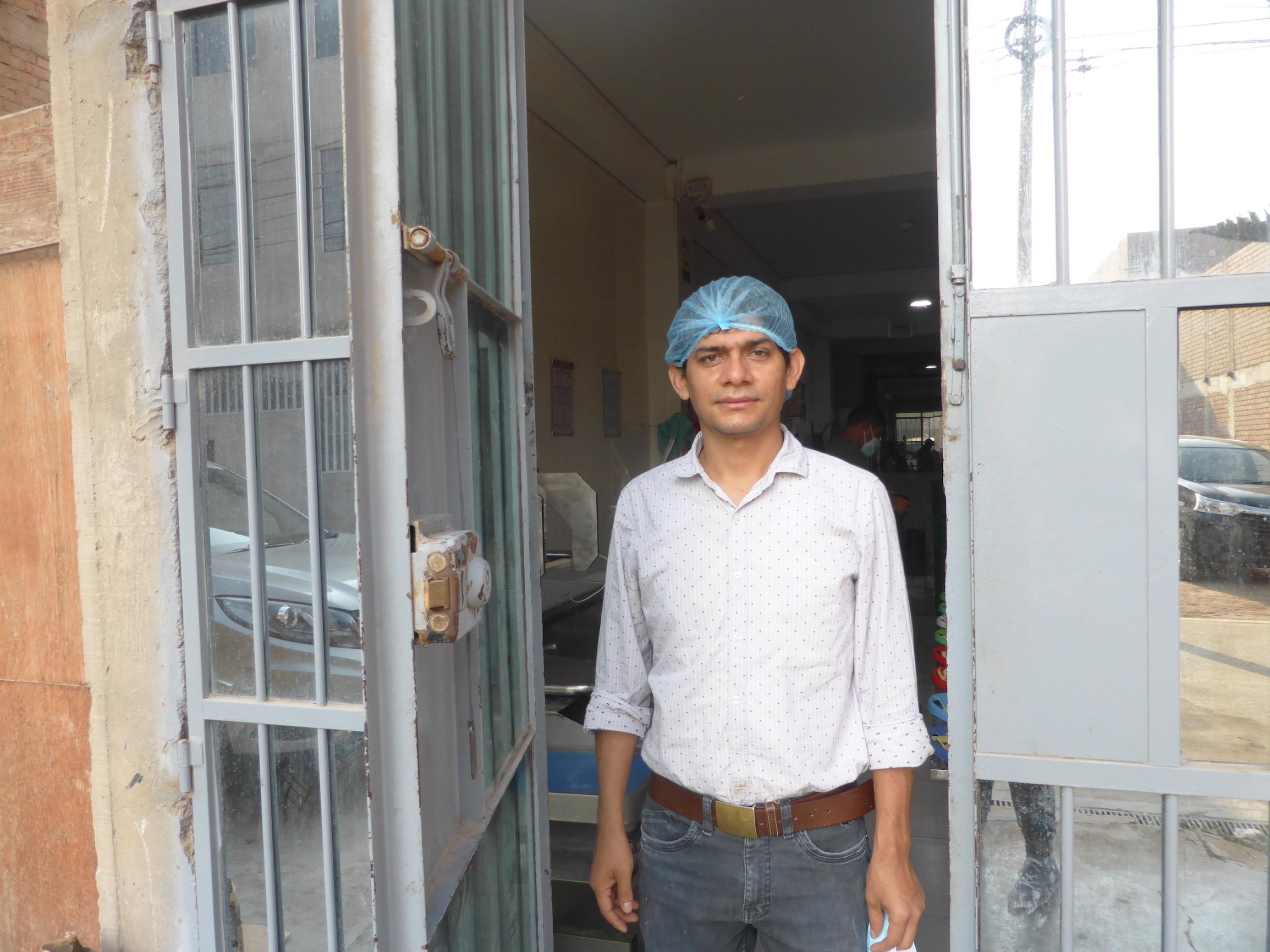 Mann in Jeans, Hemd und Haarnetz steht im Eingang einer mit Mtealltoren gesicherten Fabrikhalle.
