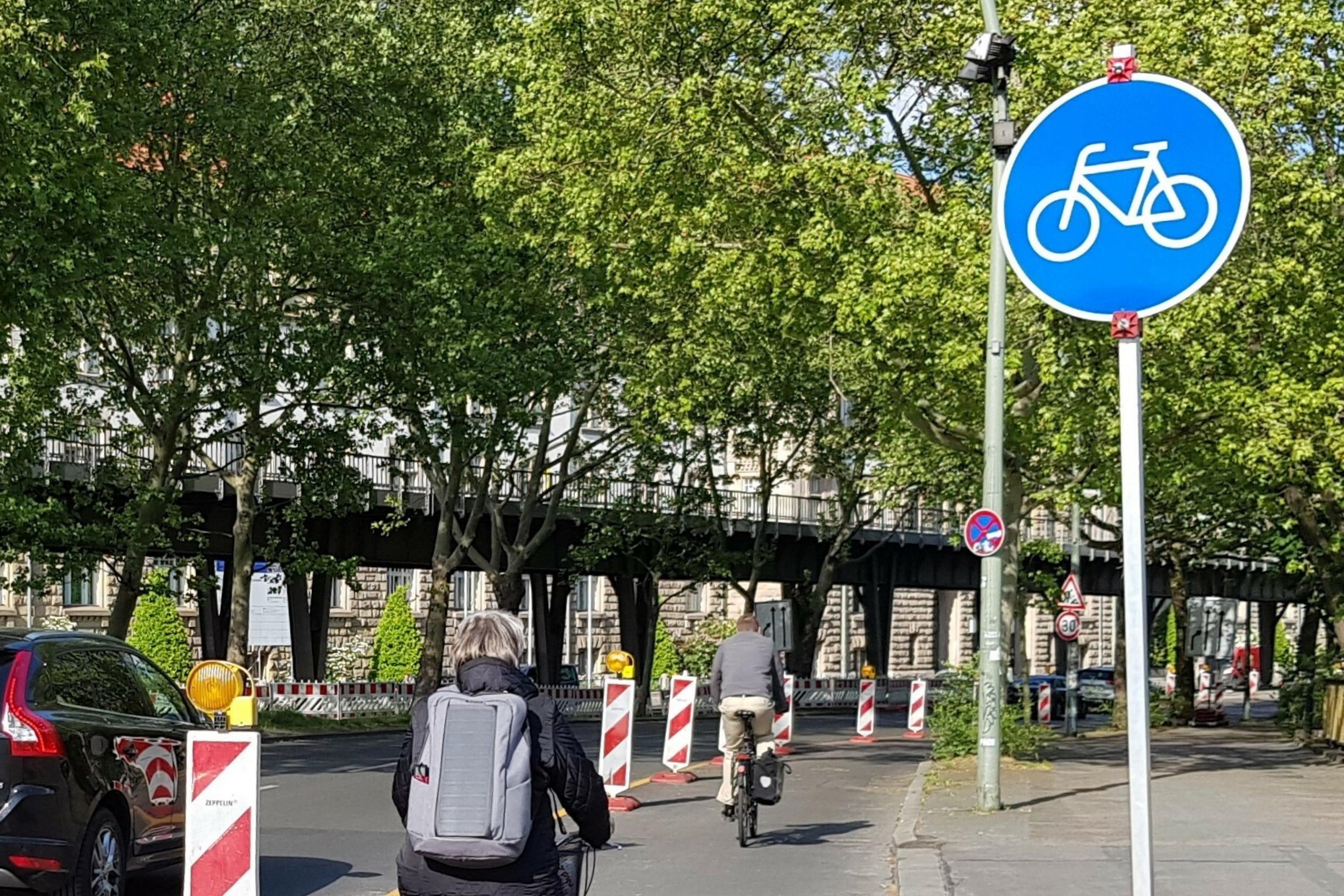 Radfahrer·innen auf einer mit Trennpfosten und gelber Markierung improvisierter Radspur in einer deutschen Stadt.