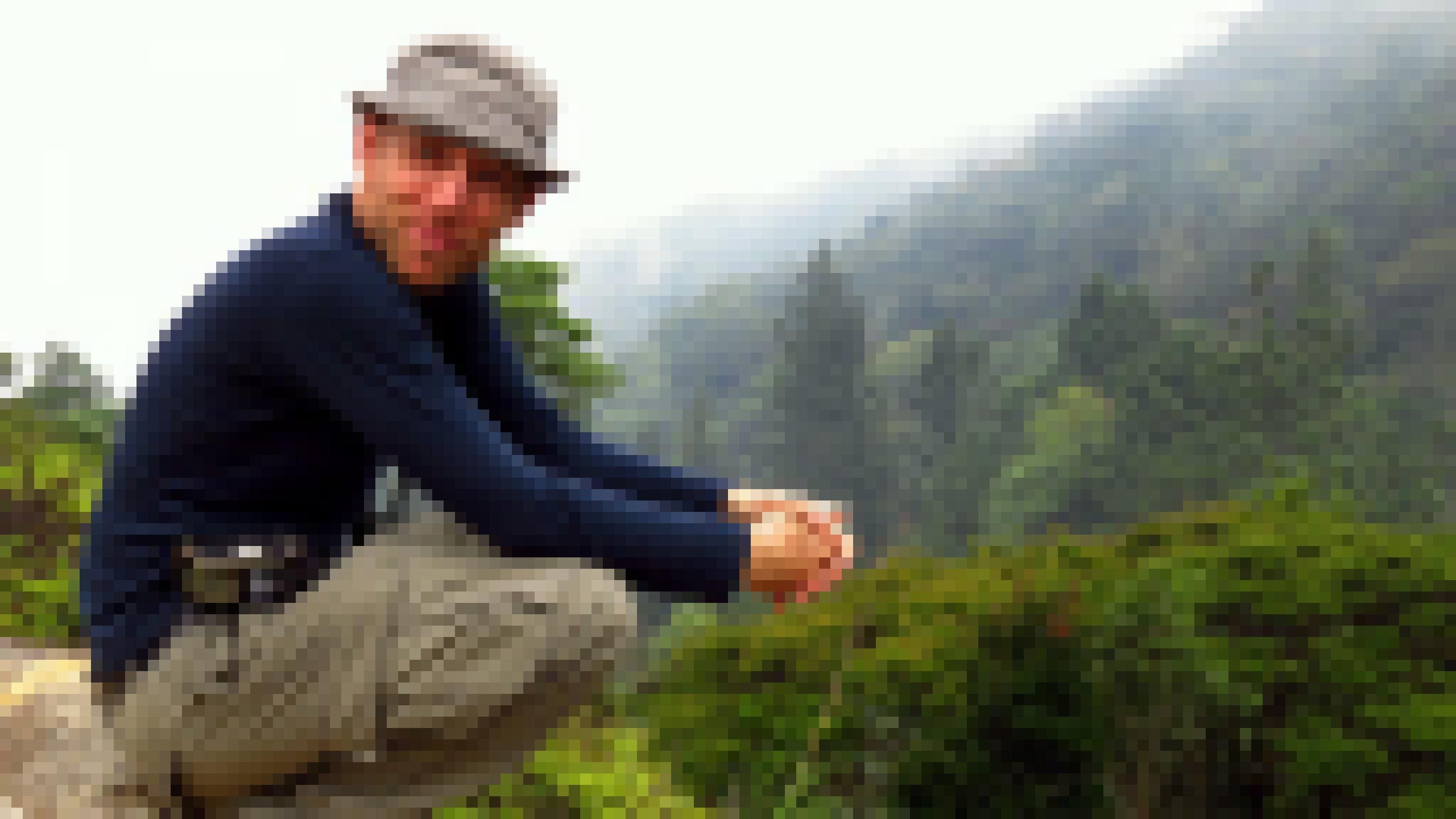 Frank Rheindt sitzt mit einem Hut auf einem Berg vor der Kulisse eines Regenwaldes