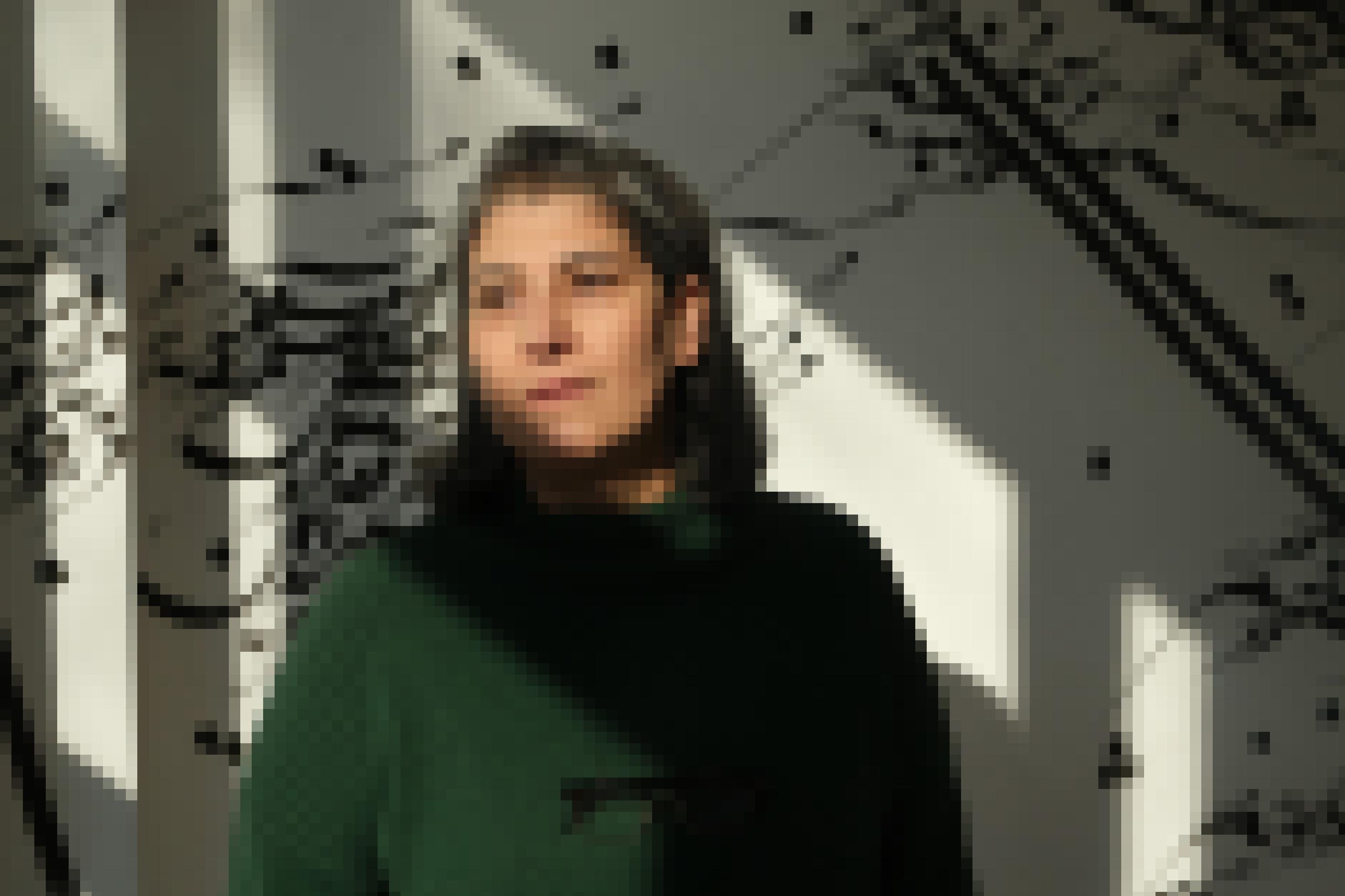Halbkörper-Porträt einer Frau mit halblangem grau-schwarzem Haar vor einer Wandzeichnung