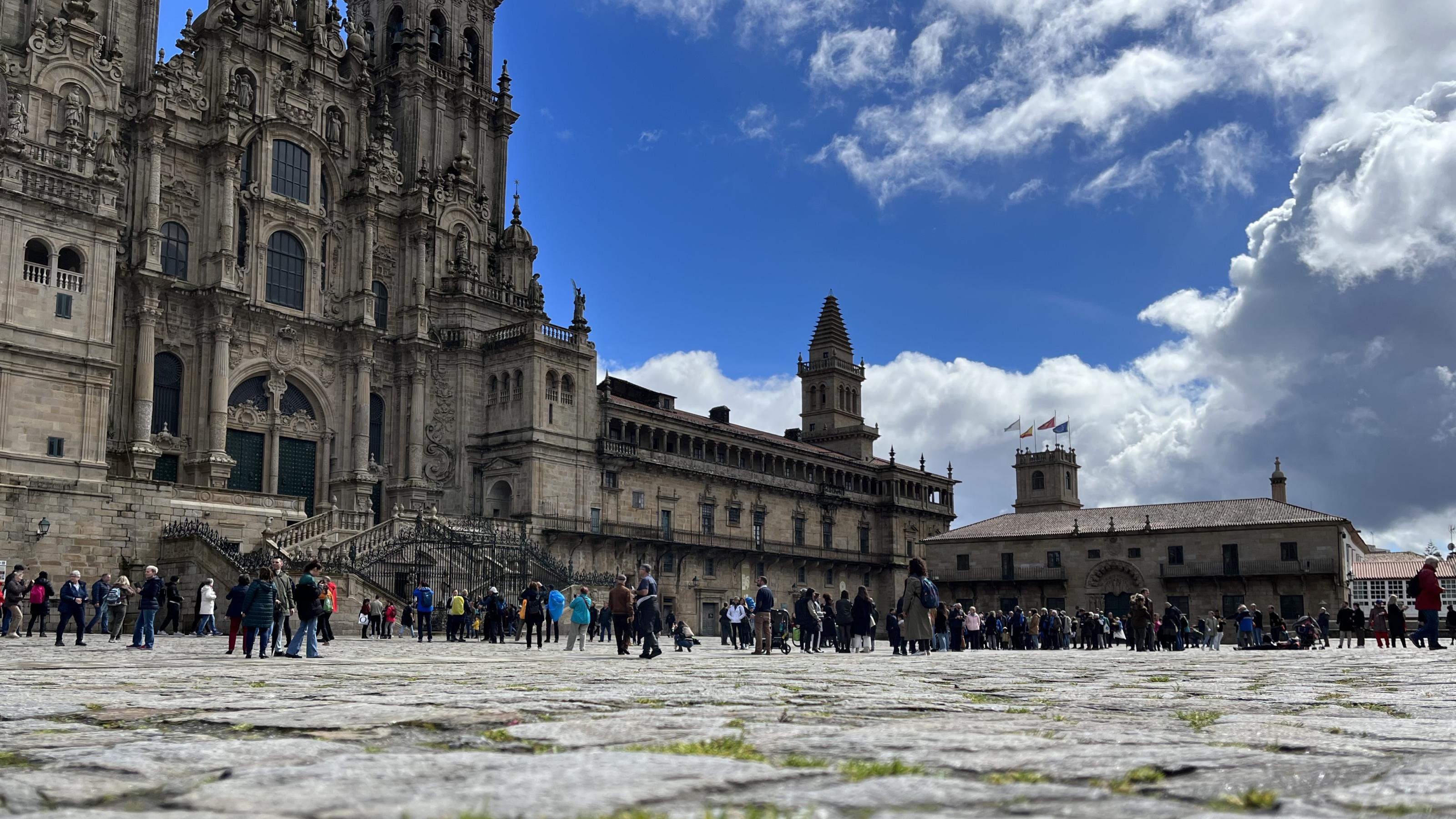 Im Vordergrund die Granitplatten der Praca do Obradoiro in Santiago de Compostela und im Hintergrund die Kathedrale vor blauem Himmel mit sich auftürmenden Wolken