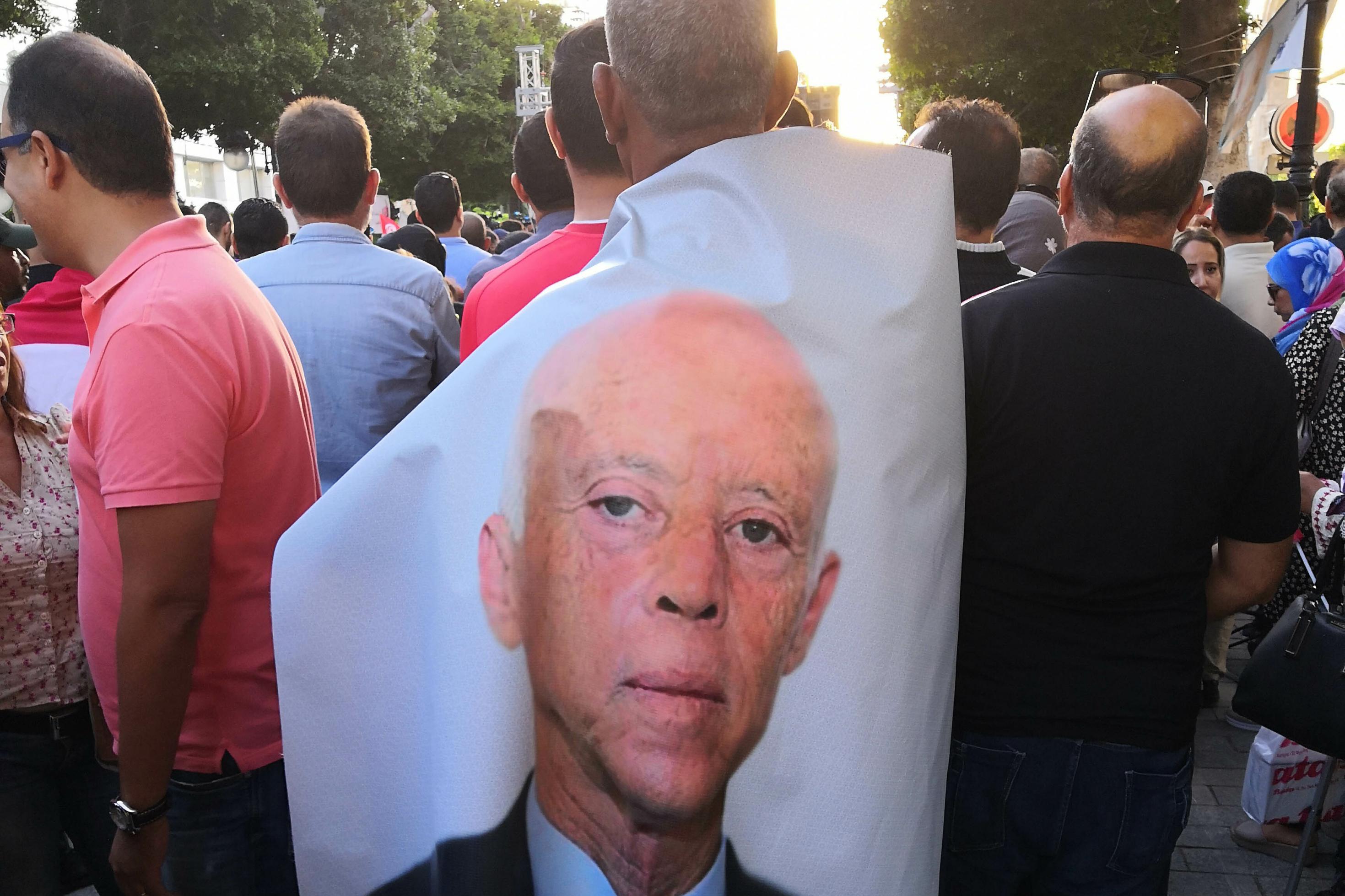 Ein Mann steht während des Präsidentschaftswahlkampfes 2019 in einer Menschenmenge auf der Ave Bourguiba der Hauptstadt Tunis. Um die Schultern geschlungen trägt er eine fast bodenlange Plane, auf der das Gesicht von Kais Saïed abgebildet ist.