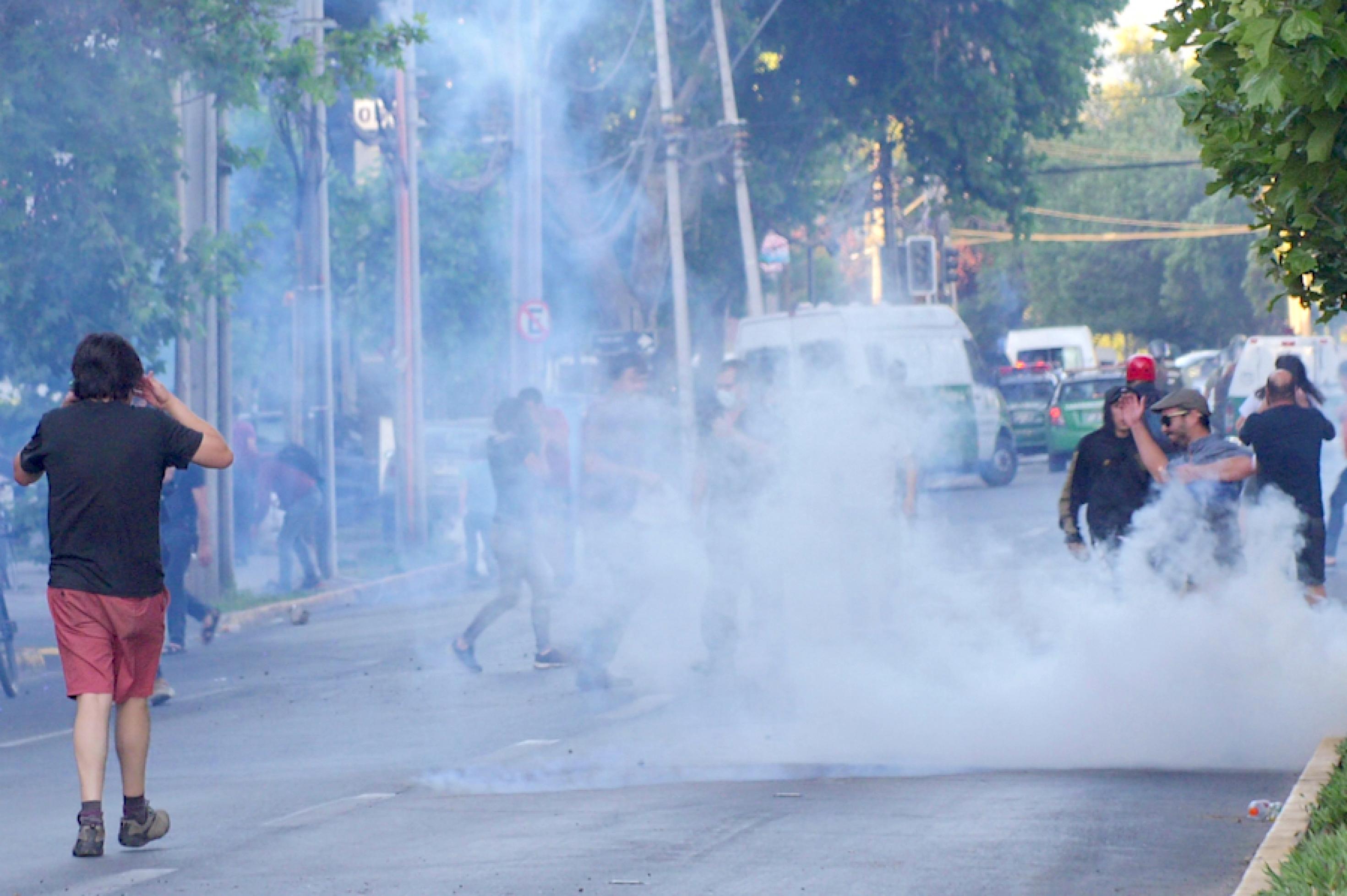 Am Rande von Protesten in Santiago de Chile fliegen Rauchbomben auf die Straße, ihm Hintergrund sind Einsatzfahrzeuge der chilenischen Polizei zu sehen.