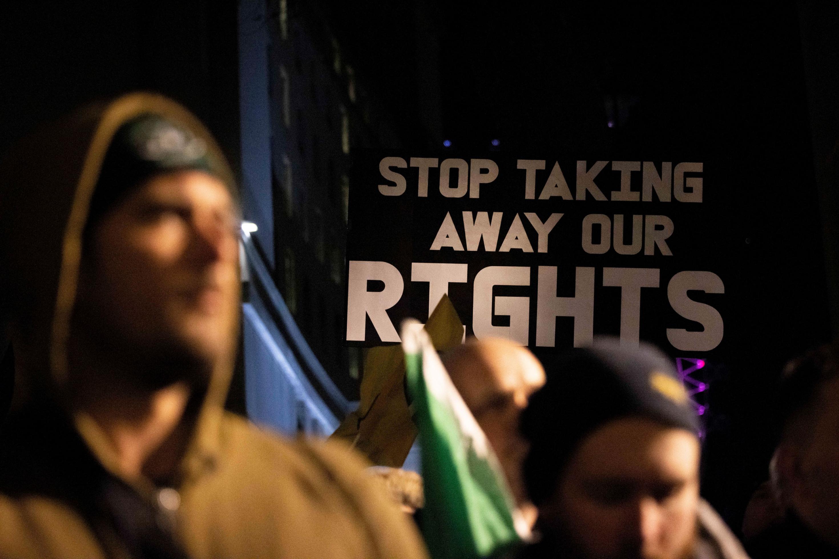 Ein Protest, auf dem ein Schild mit der Aufschrift „Stop taking away our rights“ zu sehen ist.