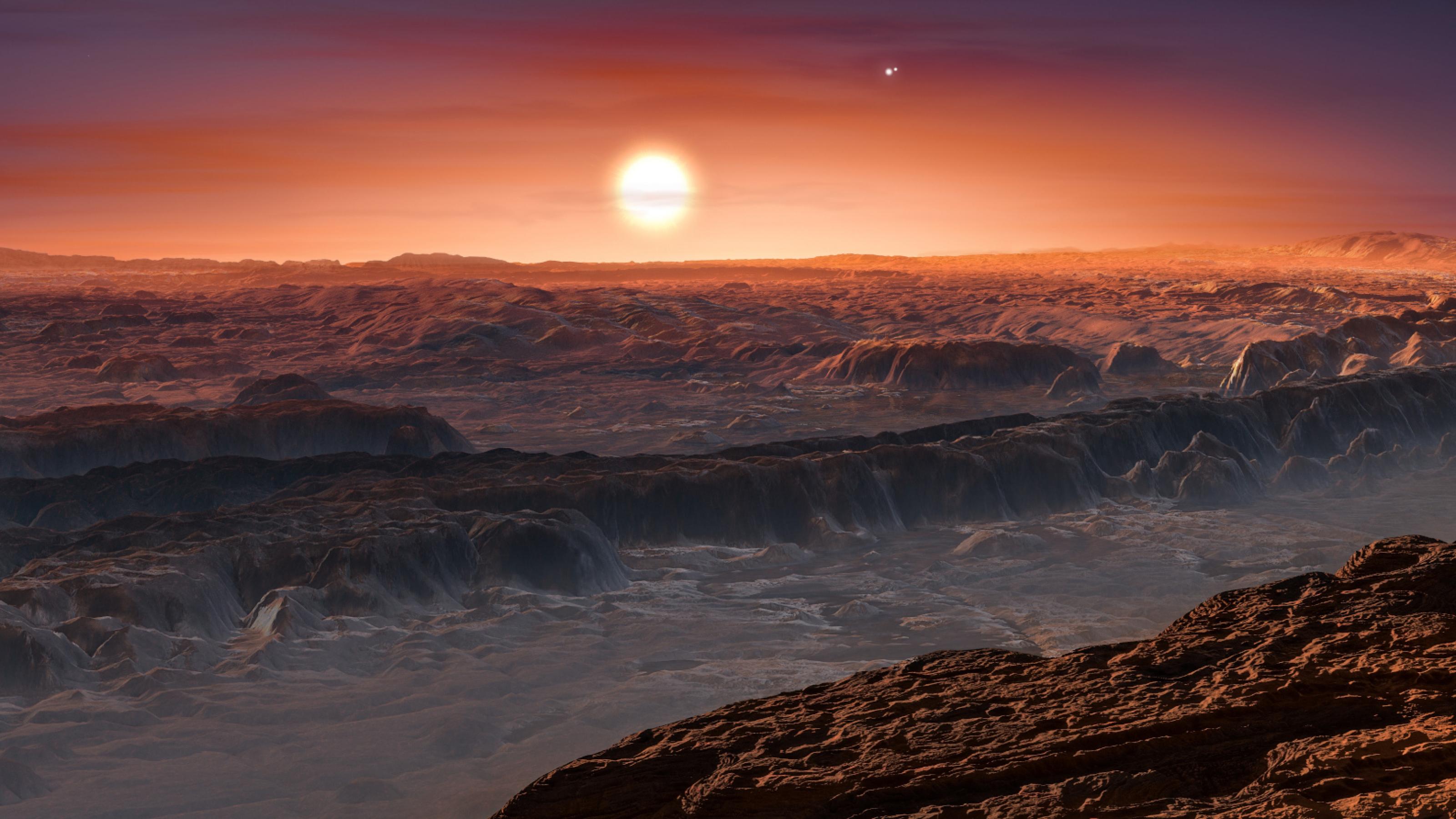 Künstlerische Darstellung der Oberfläche von Proxima b, mit Felsen und Sonnenuntergang. Der Planet umkreist den roten Zwergstern Proxima Centauri, den nächsten Stern zu unserem Sonnensystem. Der Doppelstern Alpha Centauri AB ist im Bild rechts oberhalb von Proxima Centauri abgebildet.