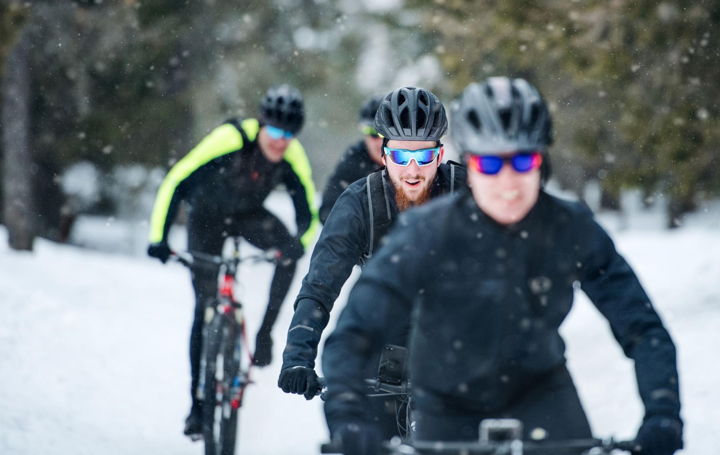 Eine Gruppe von Radfahenden fährt in Winter-Landschaft auf den Fotografen zu.