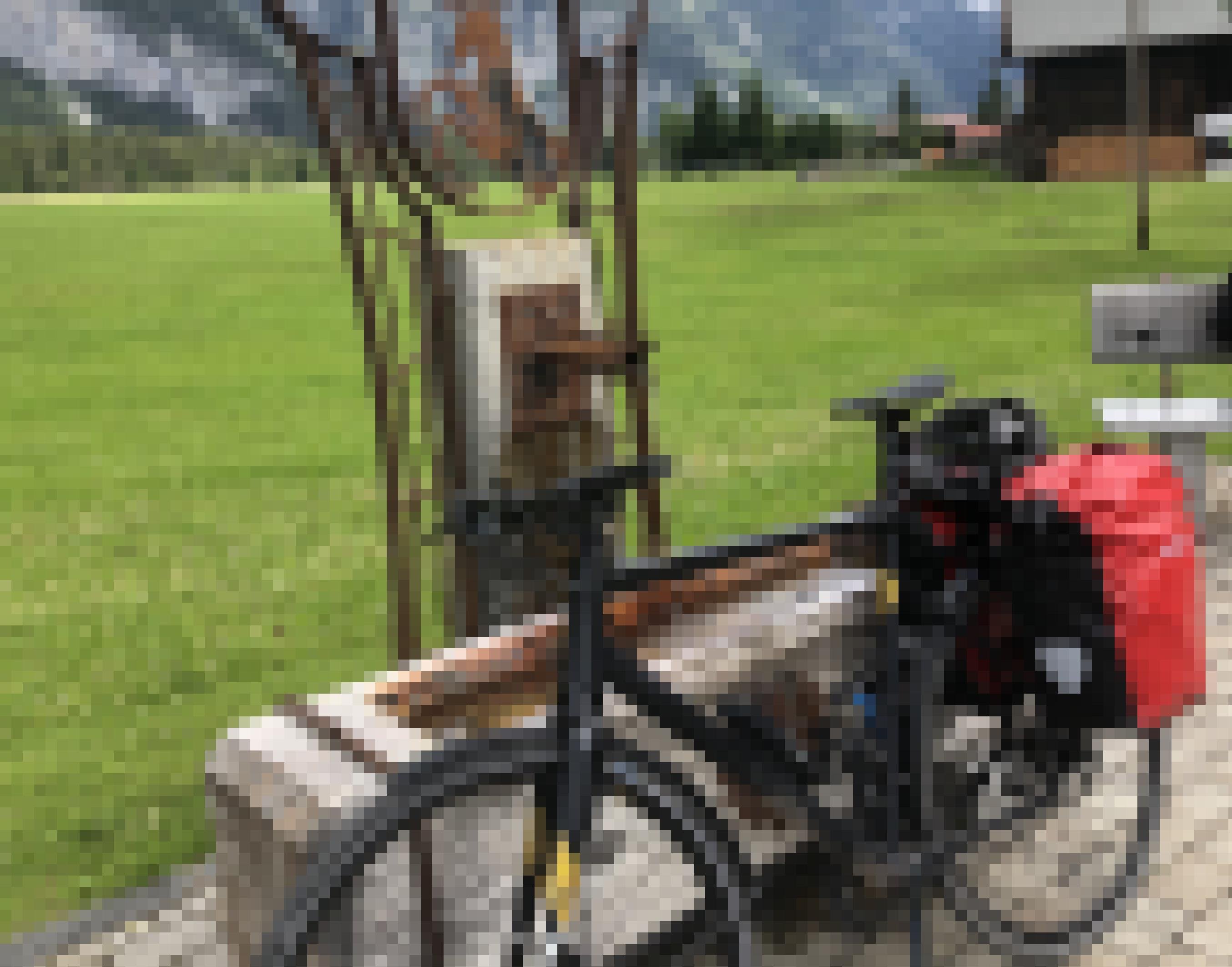 Dargestellt ist ein offener Brunnen in Tirol, aus dem Wasser fließt. Am Brunnen lehnt ein Fahrrad mit Gepäck.
