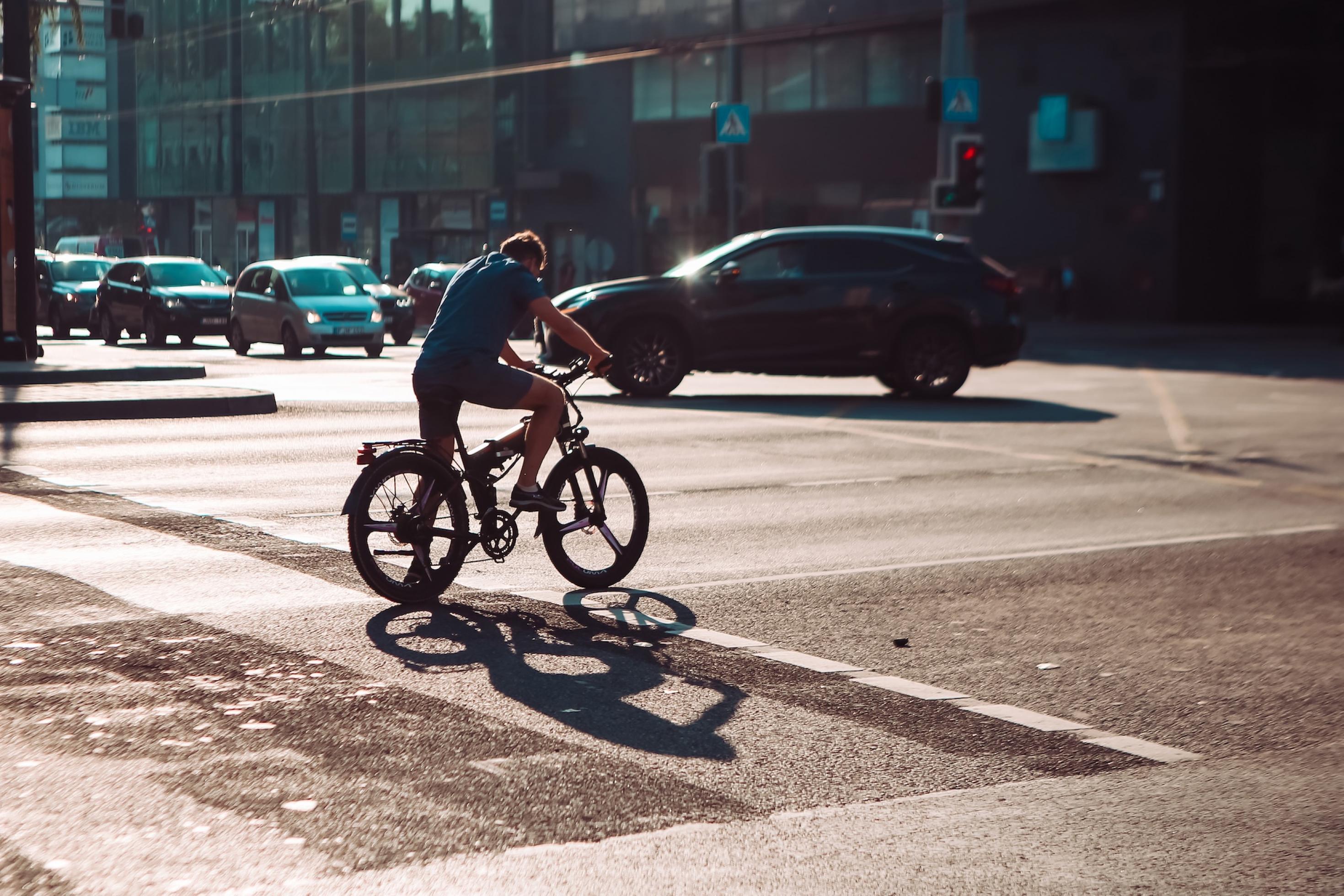 Ein Radfahrer steht an einer Kreuzung mit viel Autoverkehr.