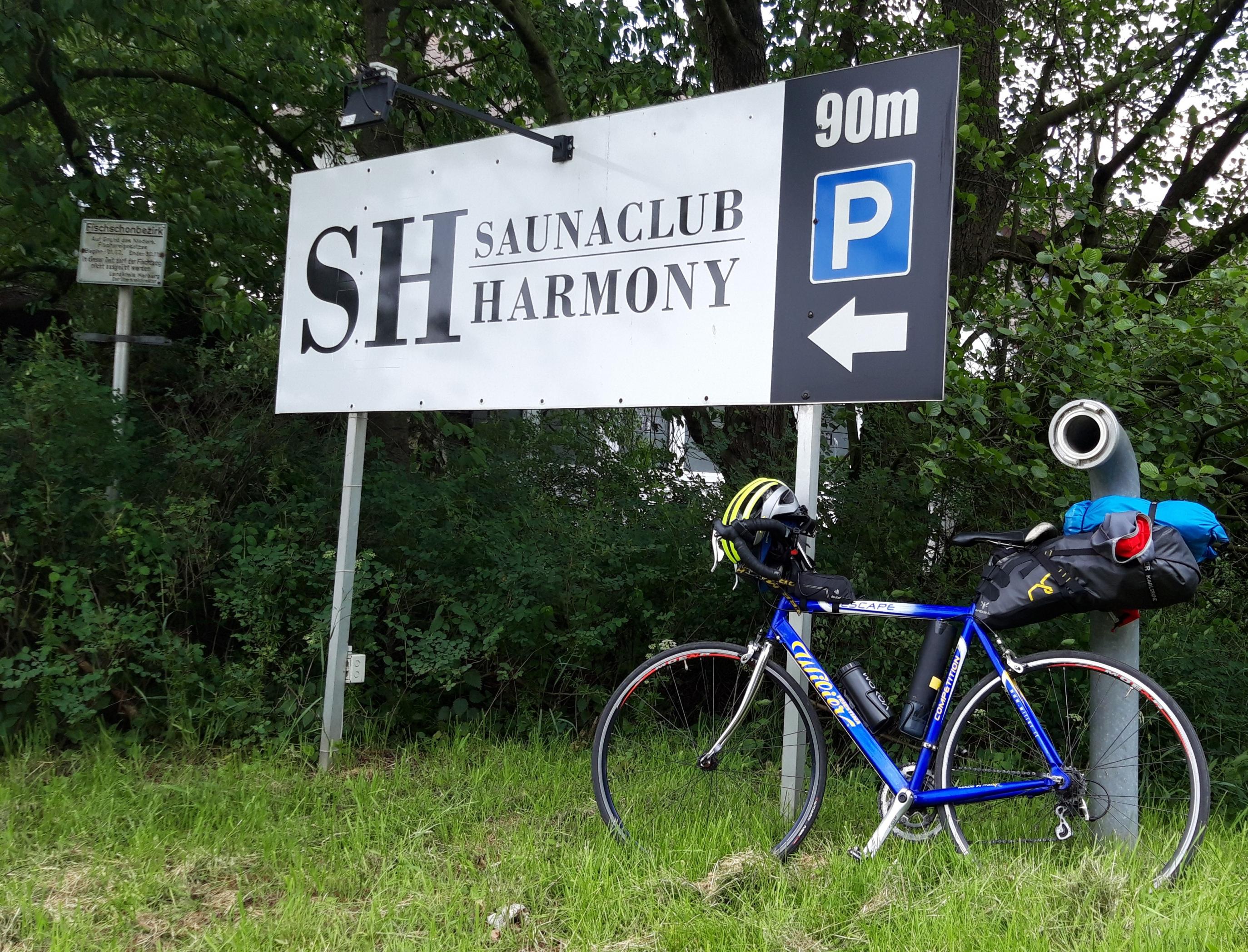 Das Vehikel des RadelndenReporters lehnt an einem Hinweisschild mit der Aufschrift Saunaclub Harmony.