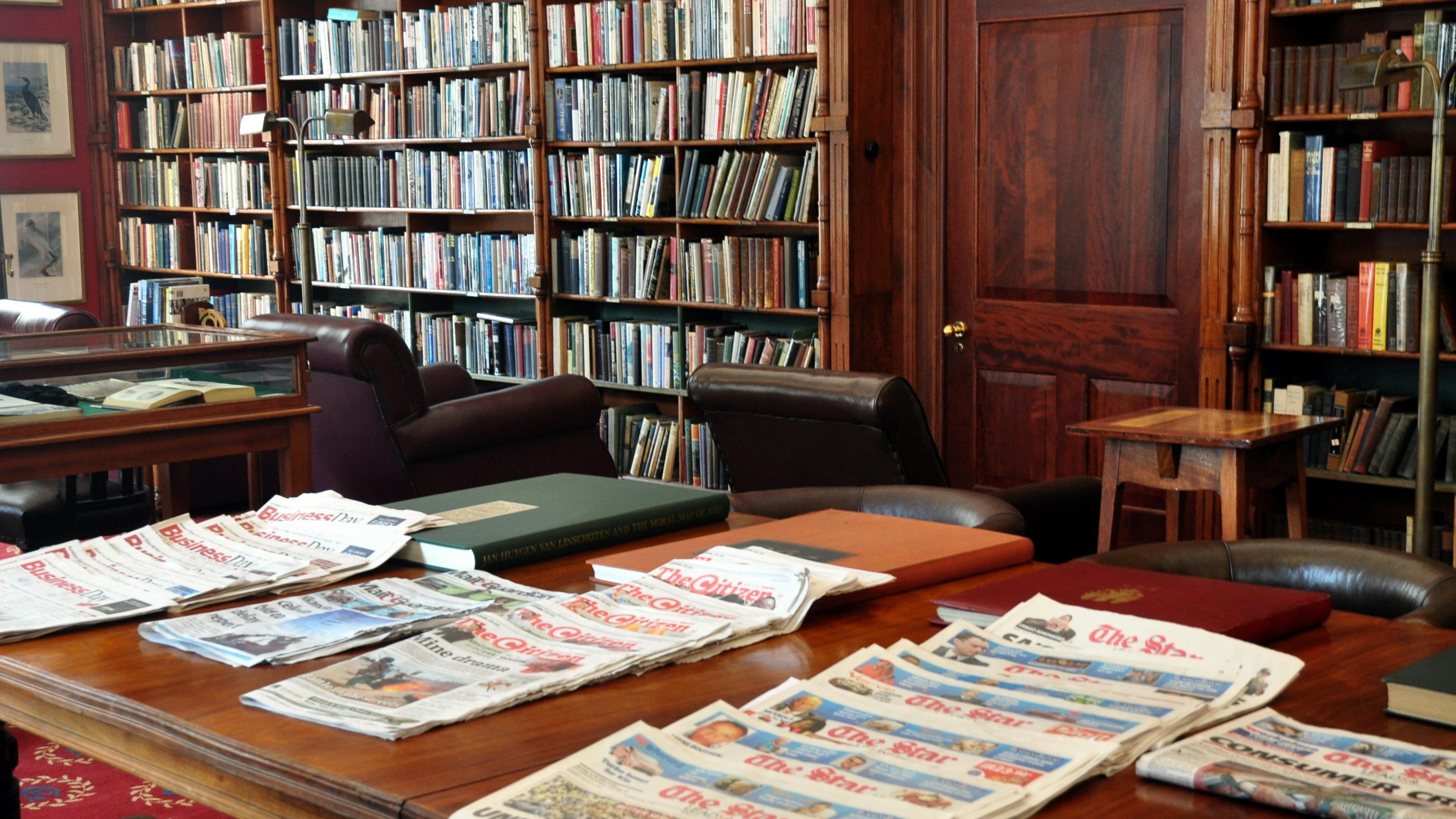Das Foto zeigt die Bibliothek des Rand Club in Johannesburg, an den Wänden hohe Bücherregale, auf dem Tisch die Zeitungsauslage.