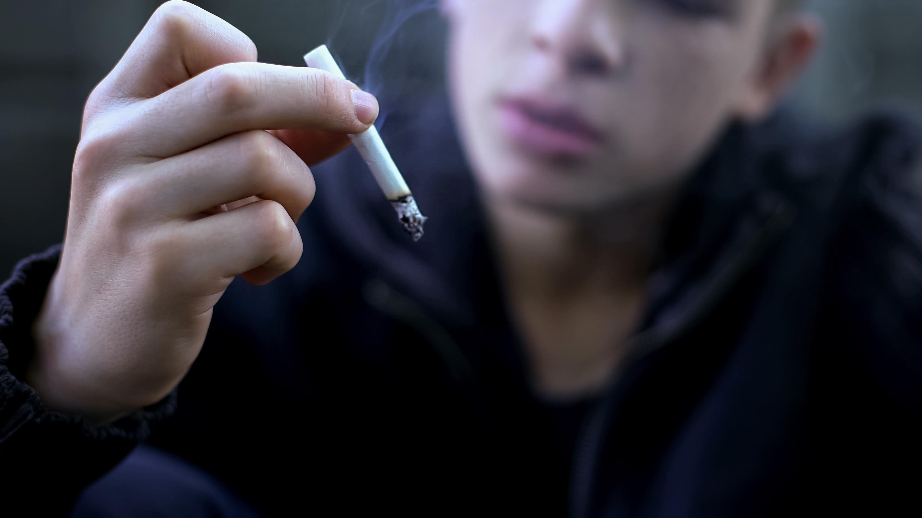 Ein Jugendlicher im schwarzen Pulli hält eine Zigarette in der Hand.
