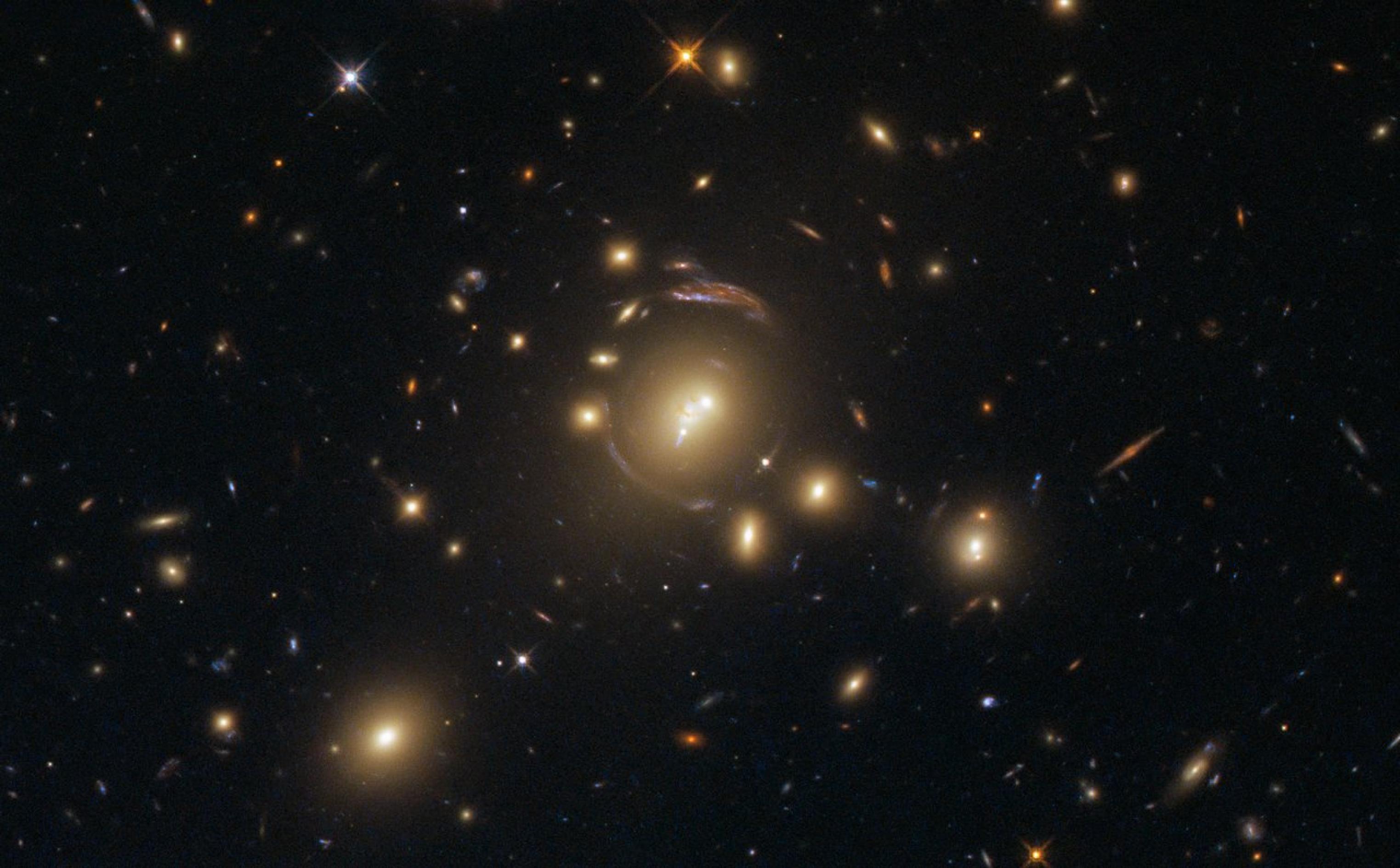 Mehrere Galaxien reihen sich zu einem regelmäßigen Muster auf: es ist ein optischer Störeffekt in Form einer Gravitationslinse, da das Licht durch eine Galaxie auf dem Weg mehrfach abgelenkt wird.