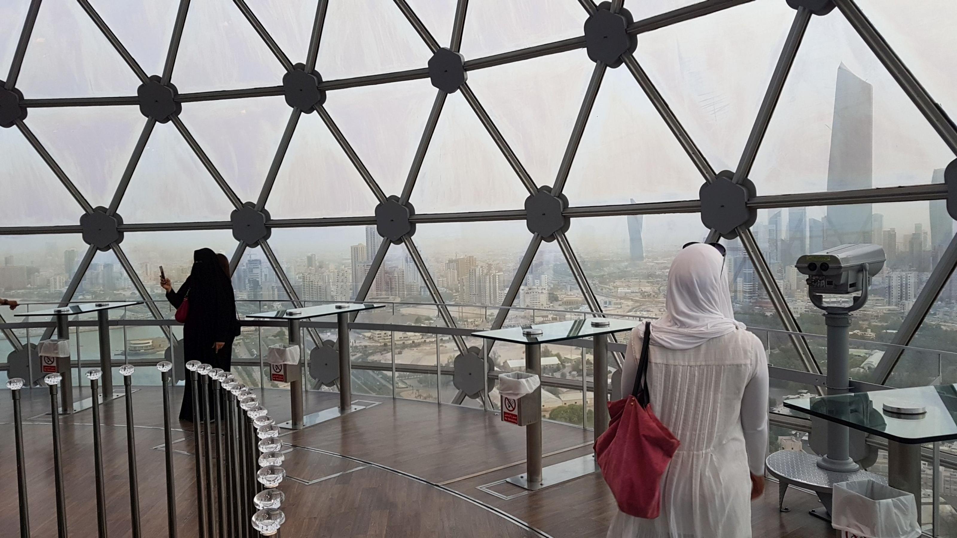 Sana steht mit dem Rücken zur Kamera unter der riesigen Glaskuppel einer Aussichtsplattform. Von dort oben kann man große Teile Kuwaits sehen.