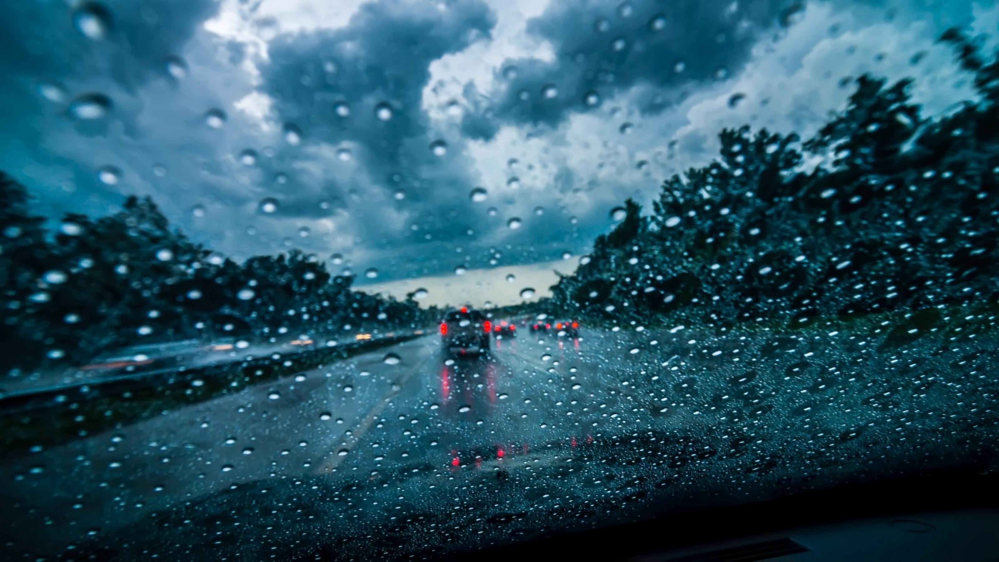Blick durch ein Autofenster voller Regentropfen auf eine dunkle Autobahn