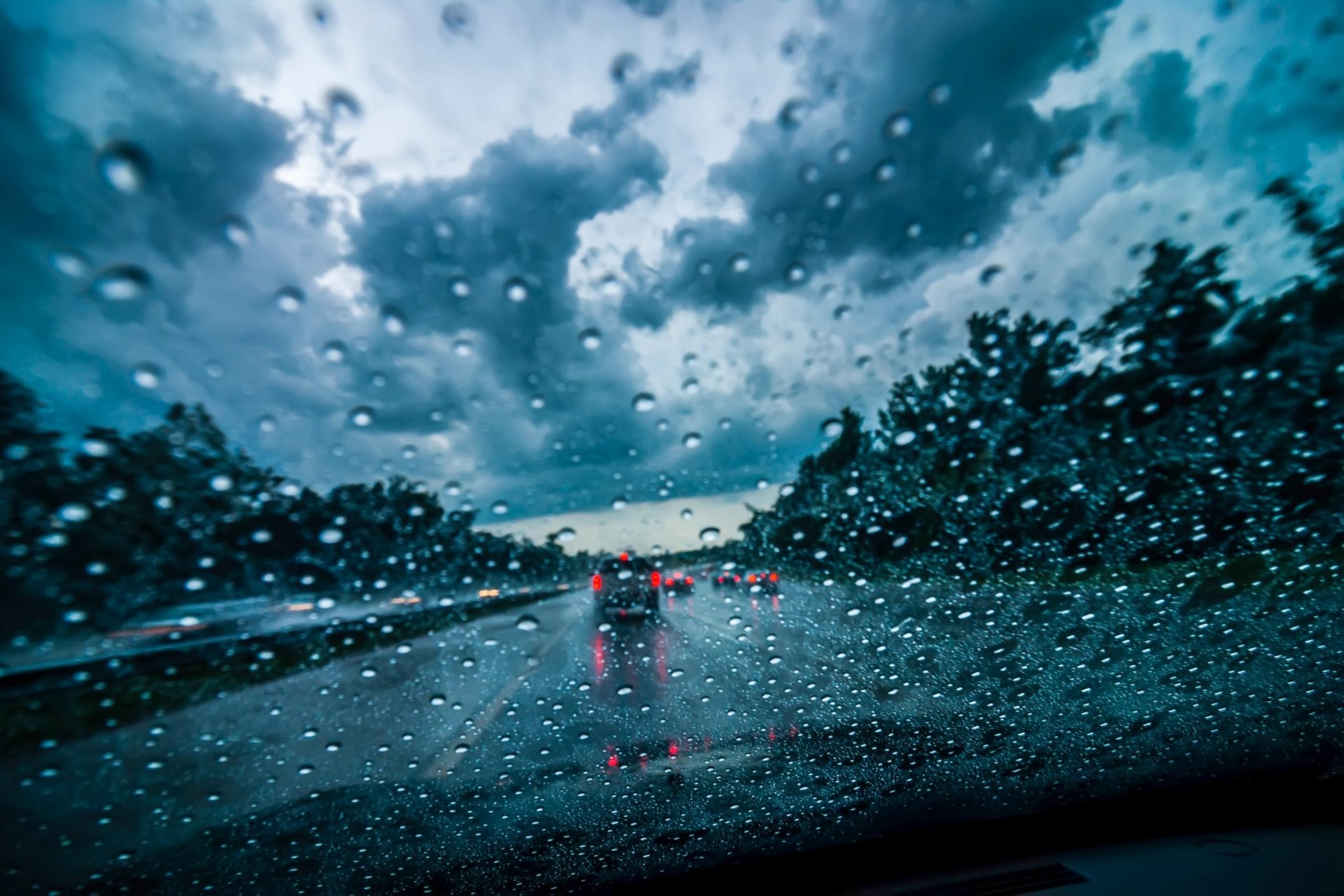 Blick durch ein Autofenster voller Regentropfen auf eine dunkle Autobahn