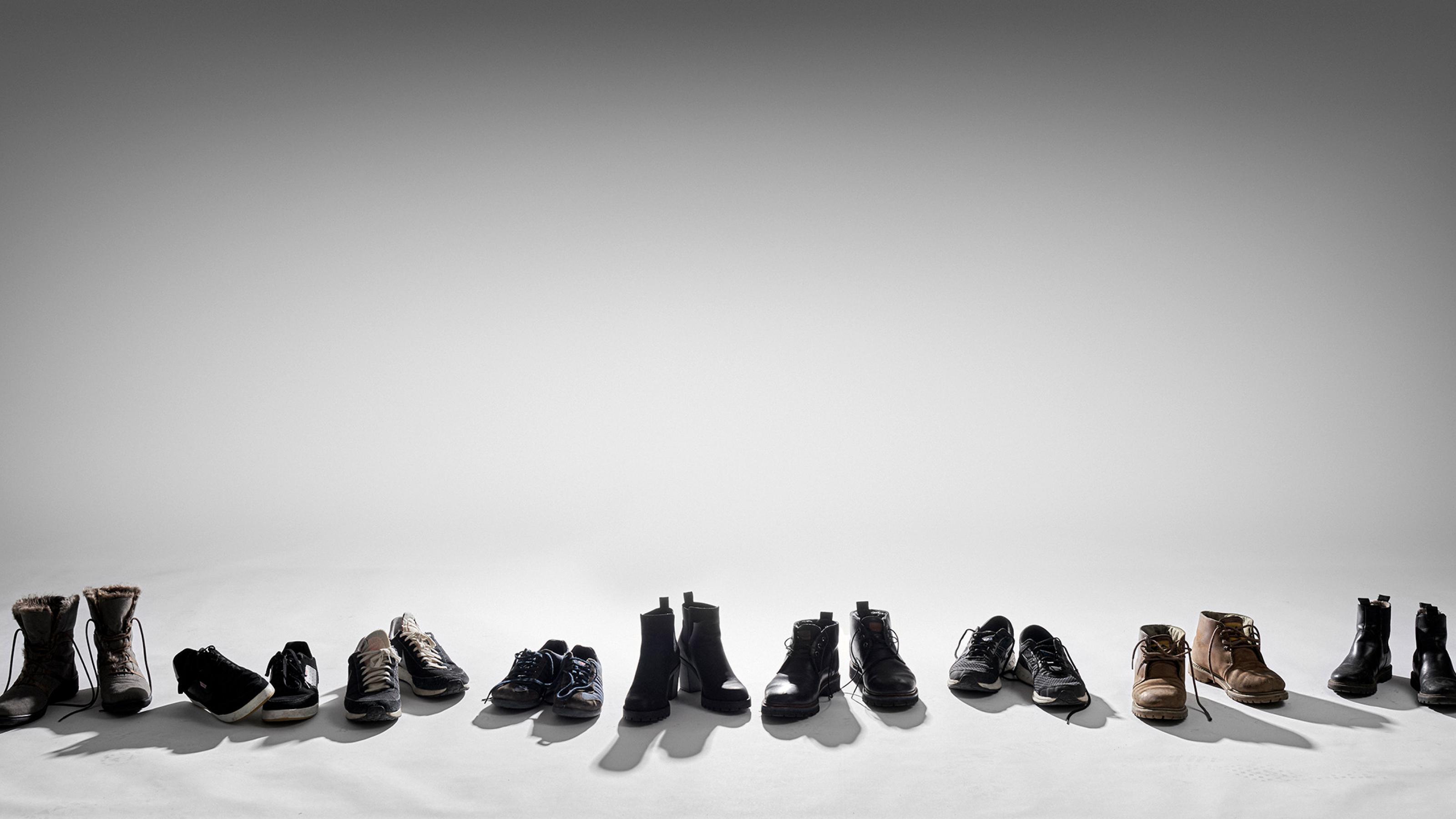 Schwarz-Weiß-Fotografie, die eine Reihe leerer Schuhpaare zeigt, mit der Spitze zum Betrachtenden gerichtet.