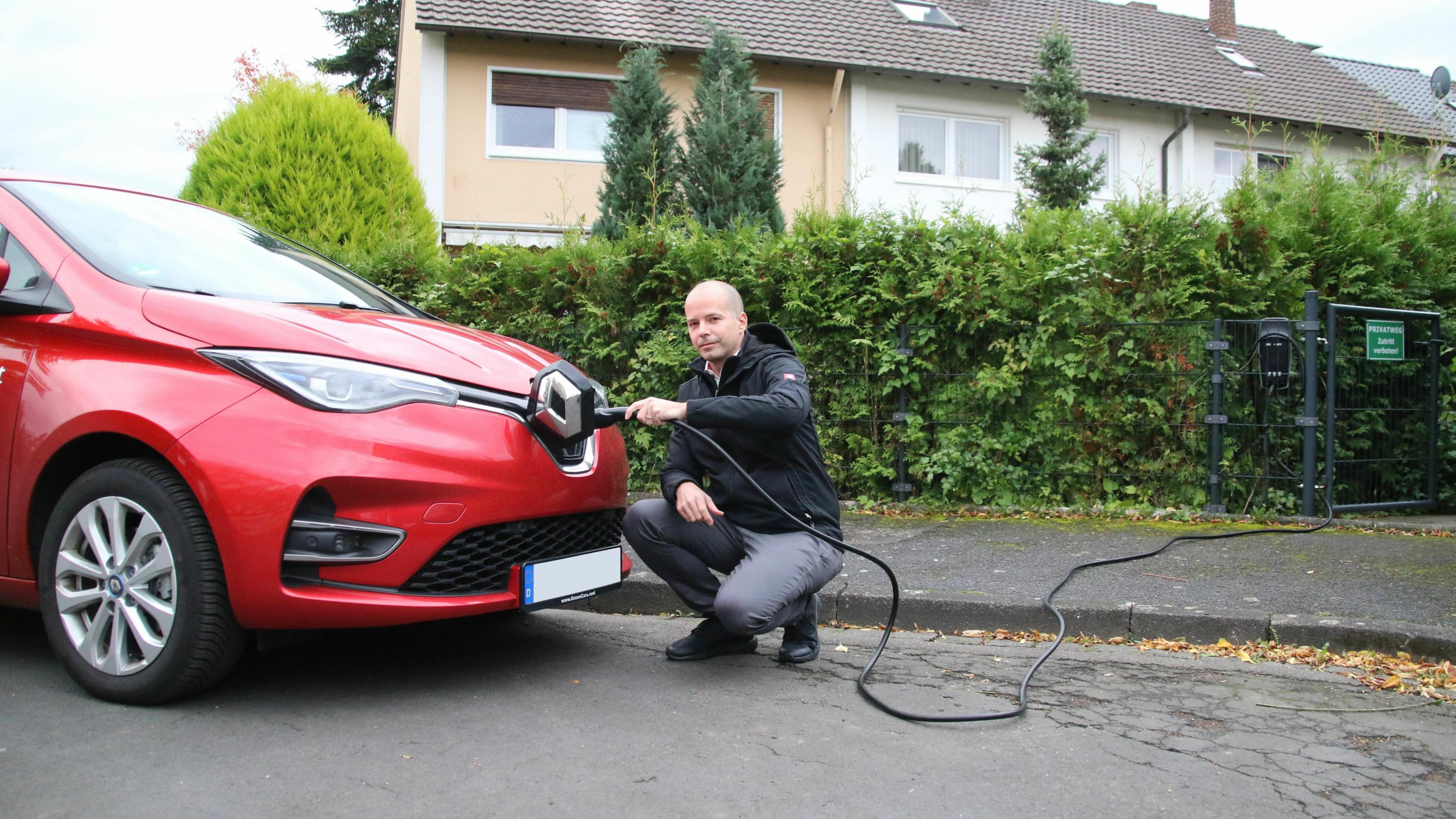 Ein Mann steckt ein Stromkabel in die Ladebuchse eines Elektroautos.