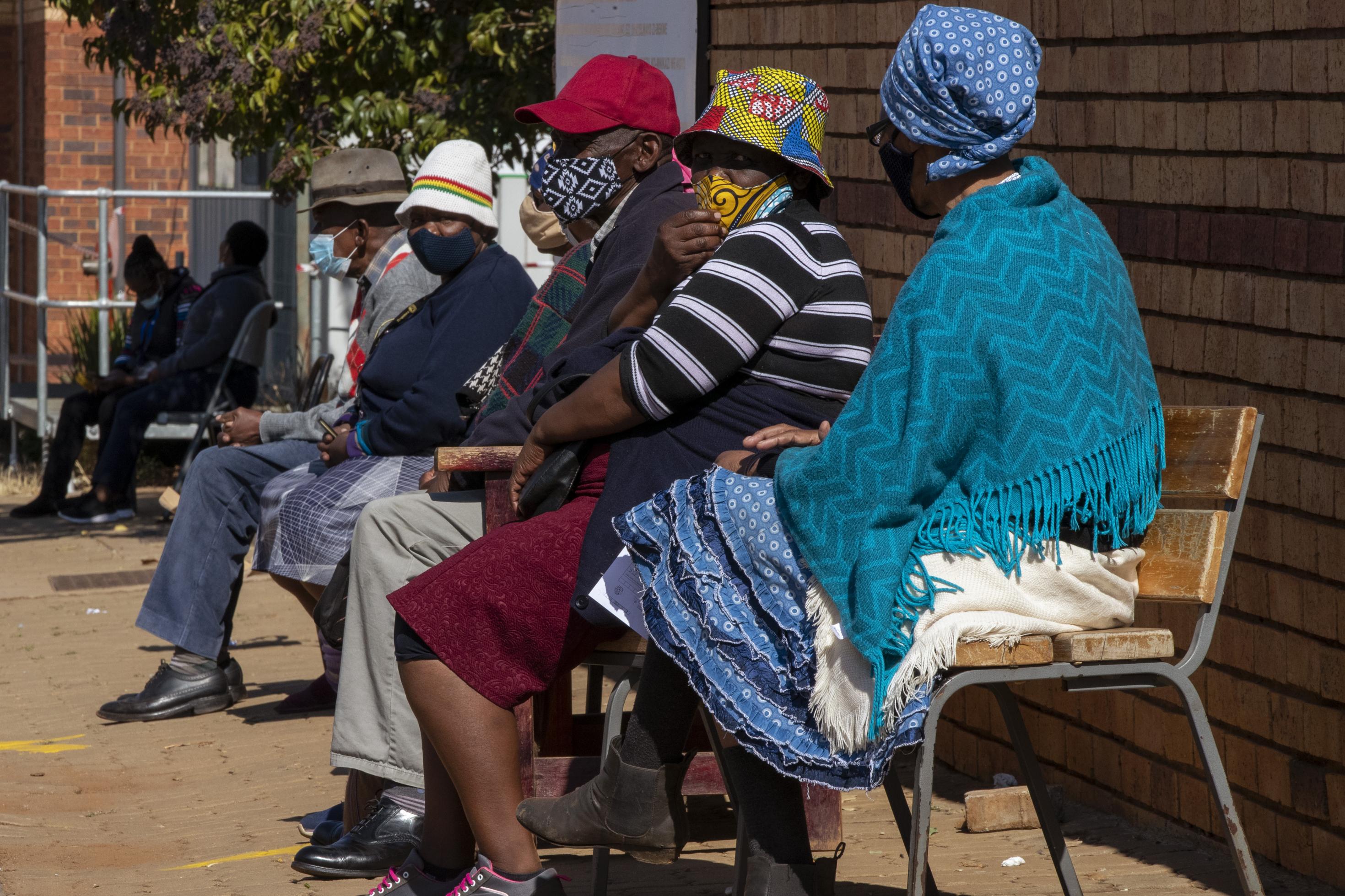 Frauen und Männer mit farbenfrohen Gesichtsmasken sitzen auf Stühlen vor der Klinik in der Schlange