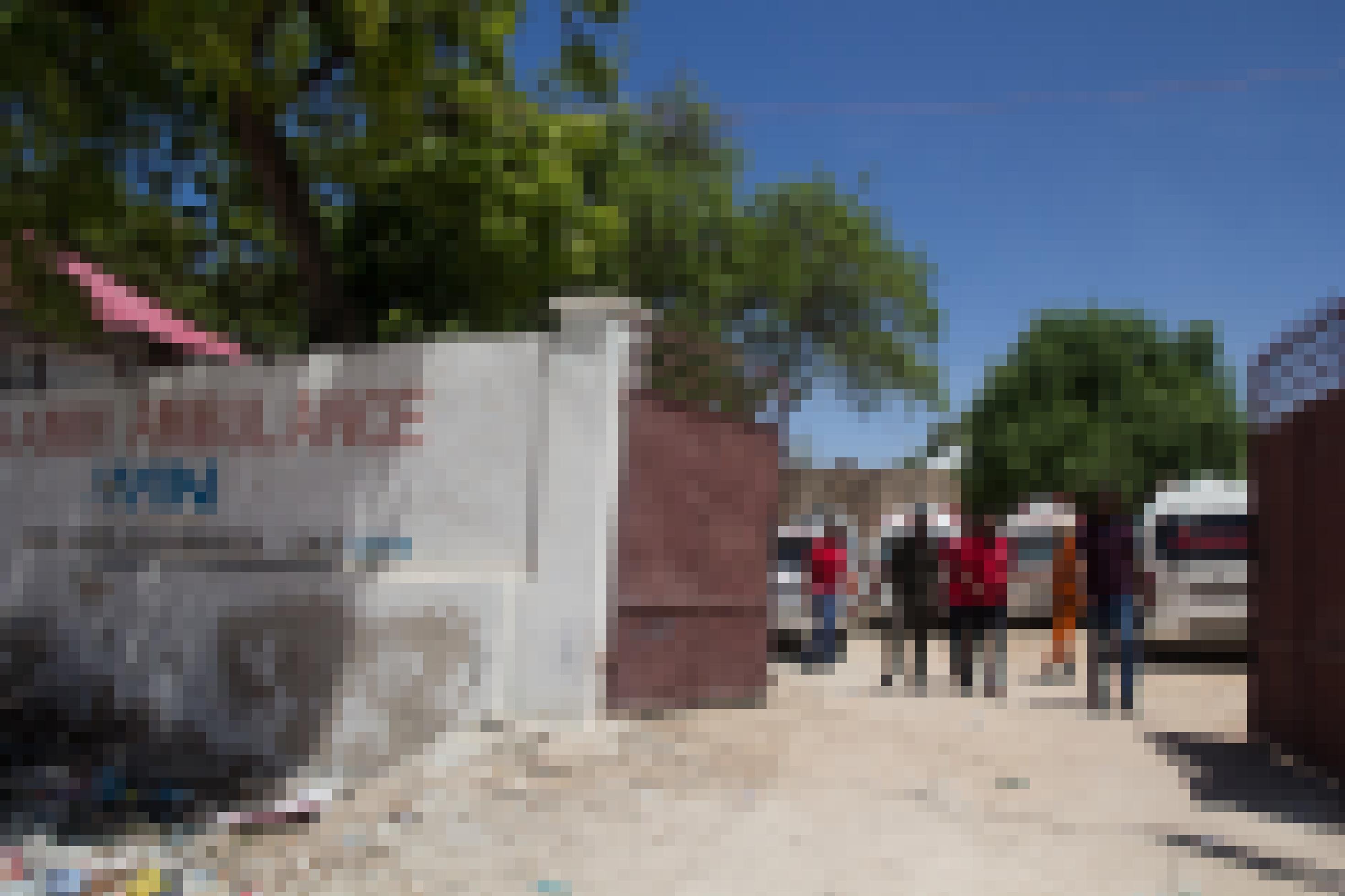 Aufnahme einer weißen Mauer mit einem geöffneten roten Tor. Auf der Wand steht „Aamin Ambulance“. Durch das geöffnete Tor sieht man mehrere Männer und einige Rettungswagen.