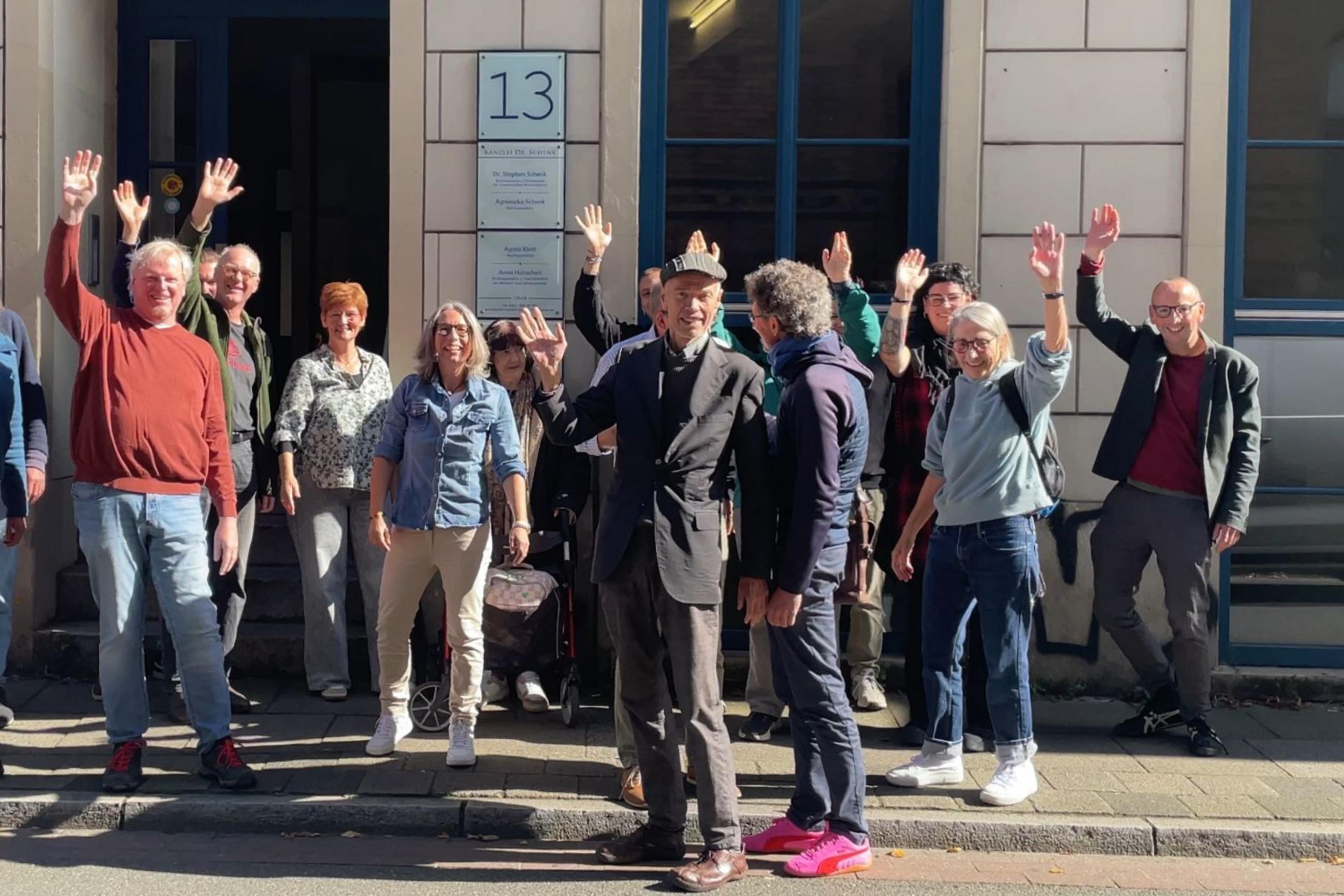 Gruppenbild mit mehreren Personen vor einem Hauseingang in Bremen, die in die Kamera winken.