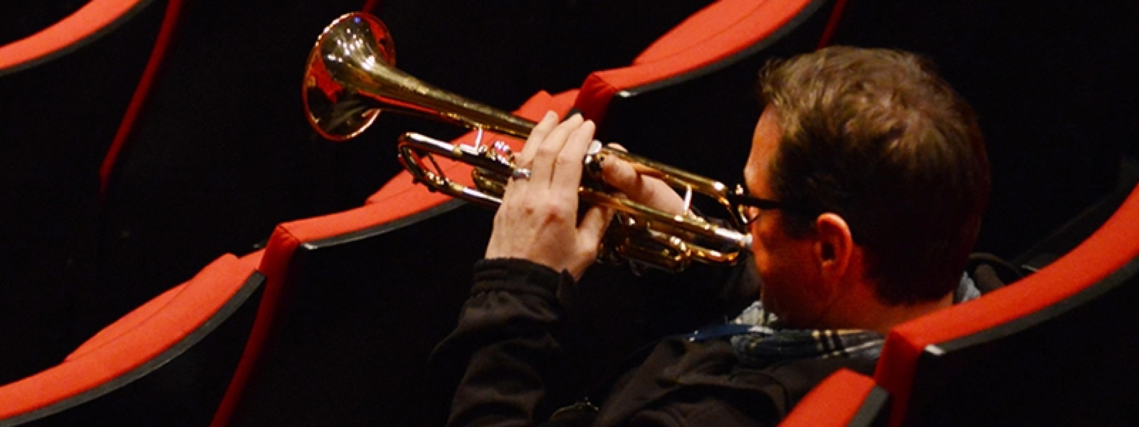 Der Trompeter der NDR Bigband, Ingolf Burkhardt, sitzt in den Rängen eines leeren Konzertsaals und bläst sein Instrument.