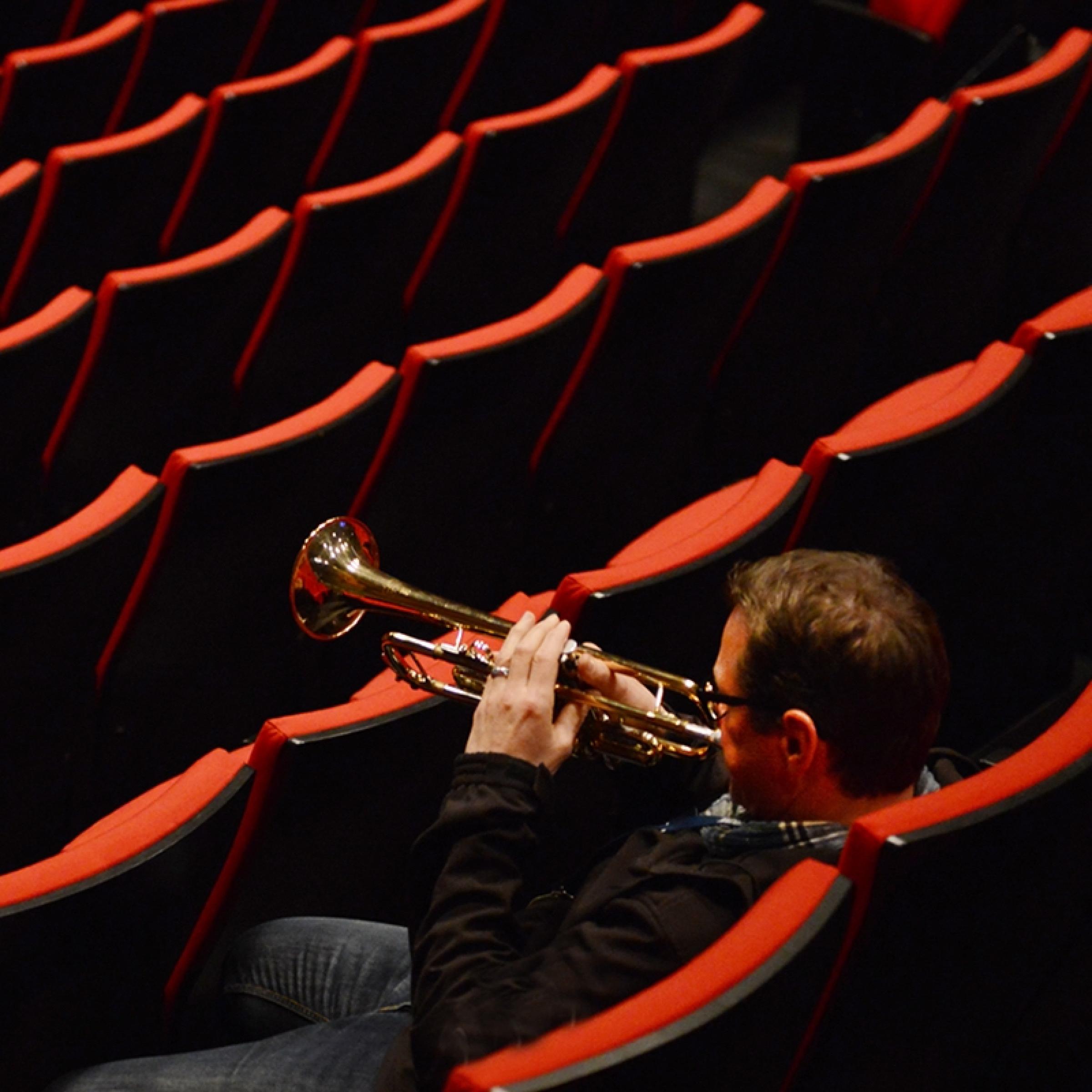 Der Trompeter der NDR Bigband, Ingolf Burkhardt, sitzt in den Rängen eines leeren Konzertsaals und bläst sein Instrument.