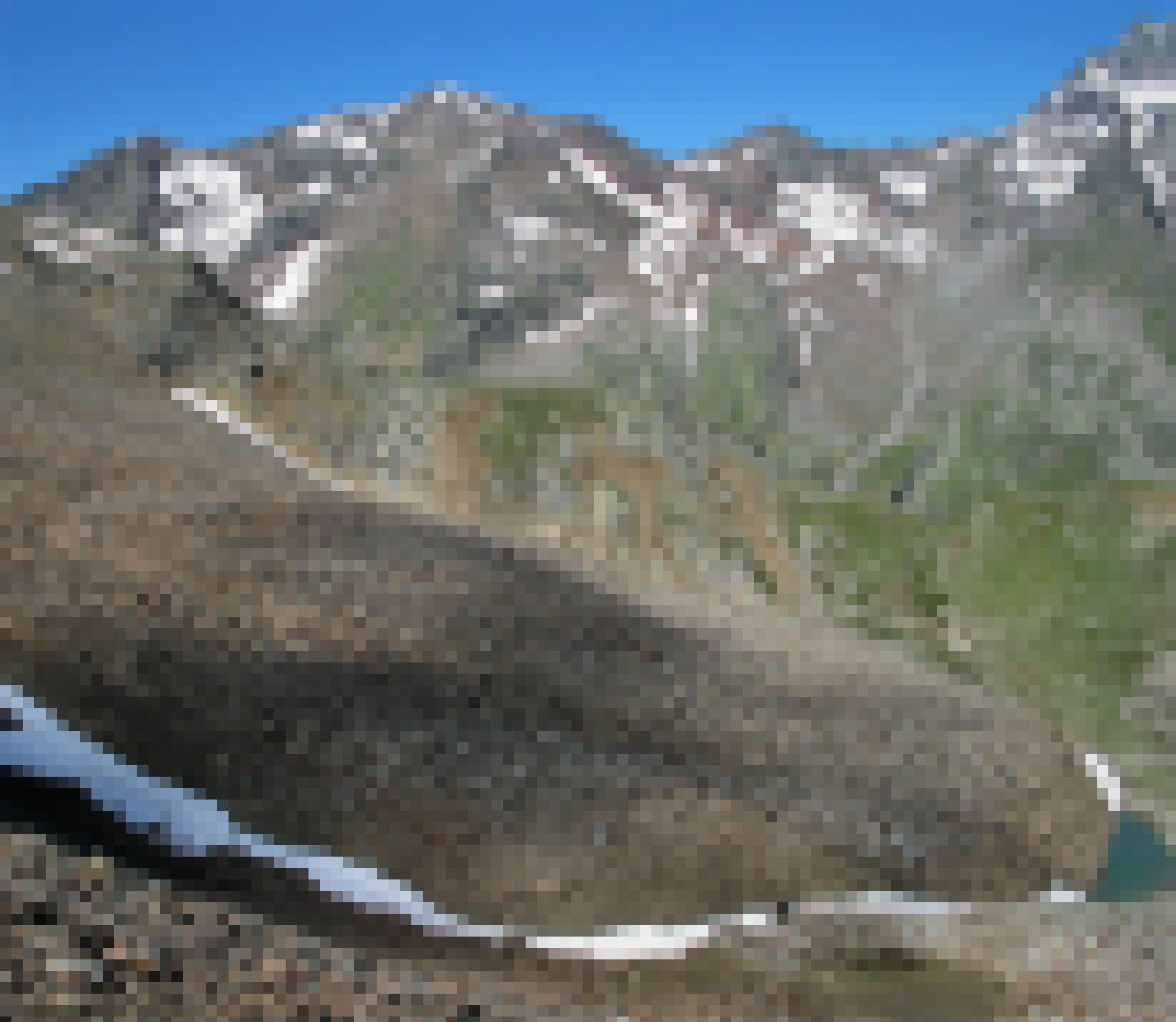 Vor einem Gipfelpanorama erstreckt sich eine lange Geröllzunge gen Tal, an deren Spitze sich Schmelzwasser sammelt.