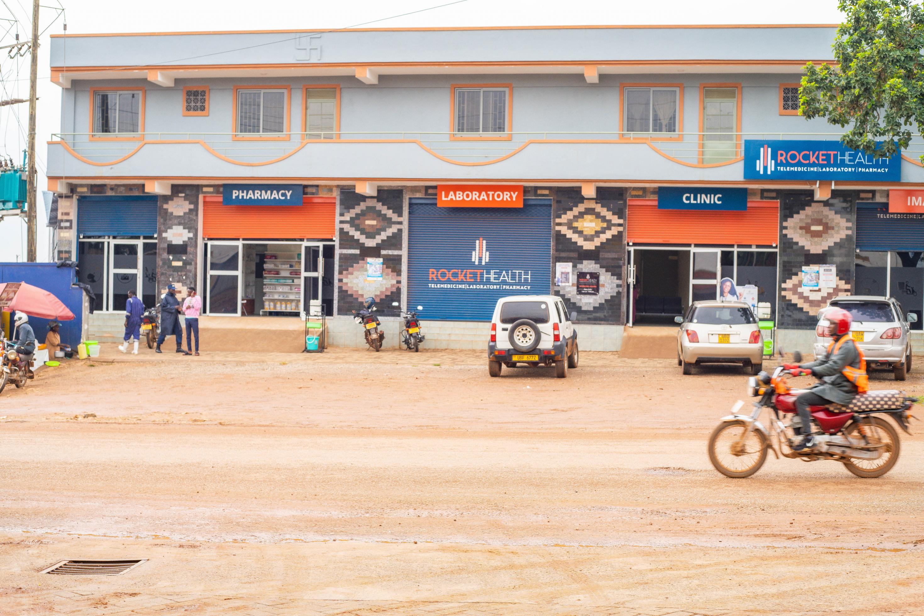 Die Fassade der Klinik ist orange und rot, auf der Straße davor fährt ein Motorrad.