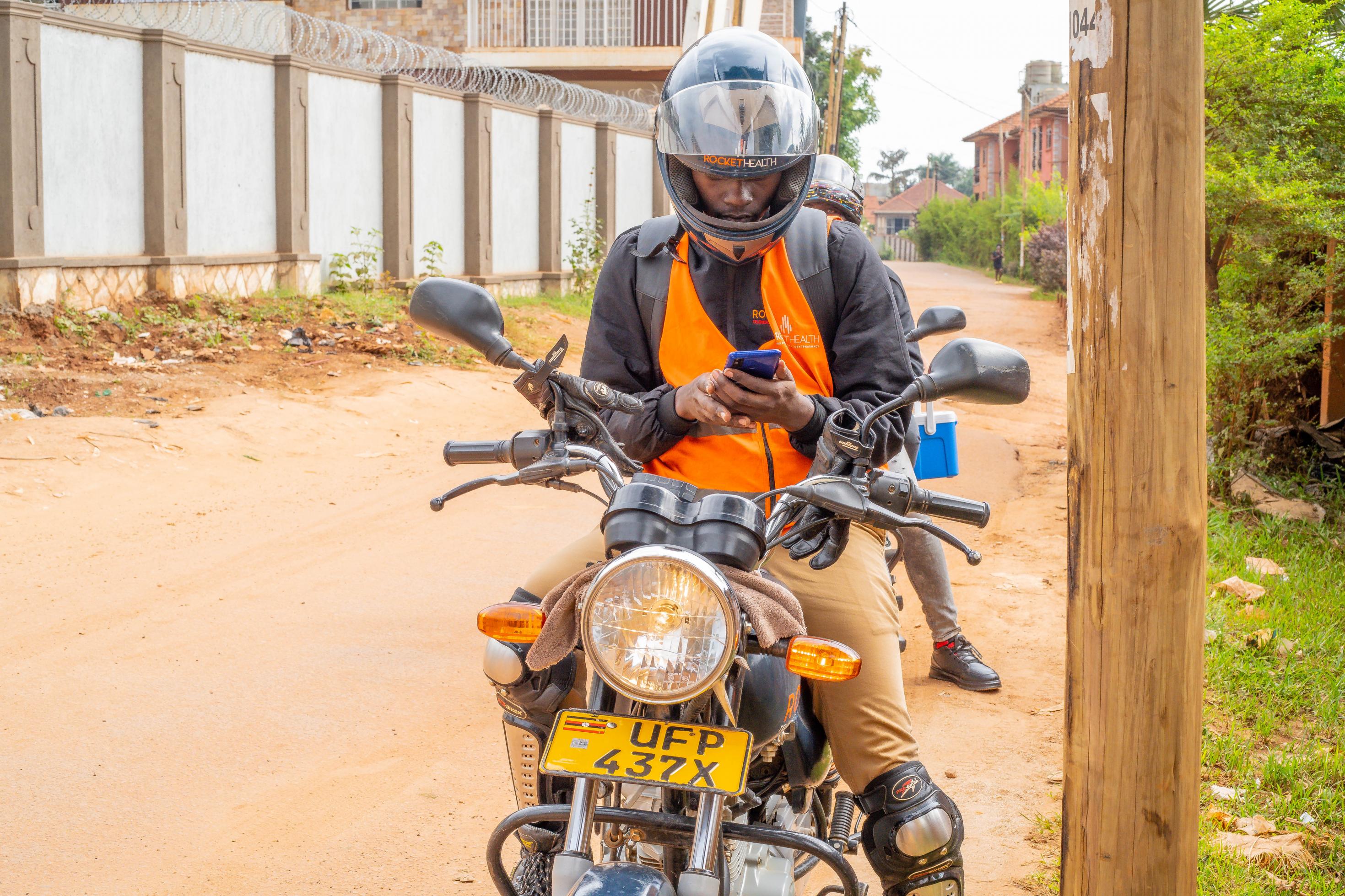 Ainemaani sitzt mit Helm auf dem Motorrad und tippt in sein Handy, bevor er losfährt