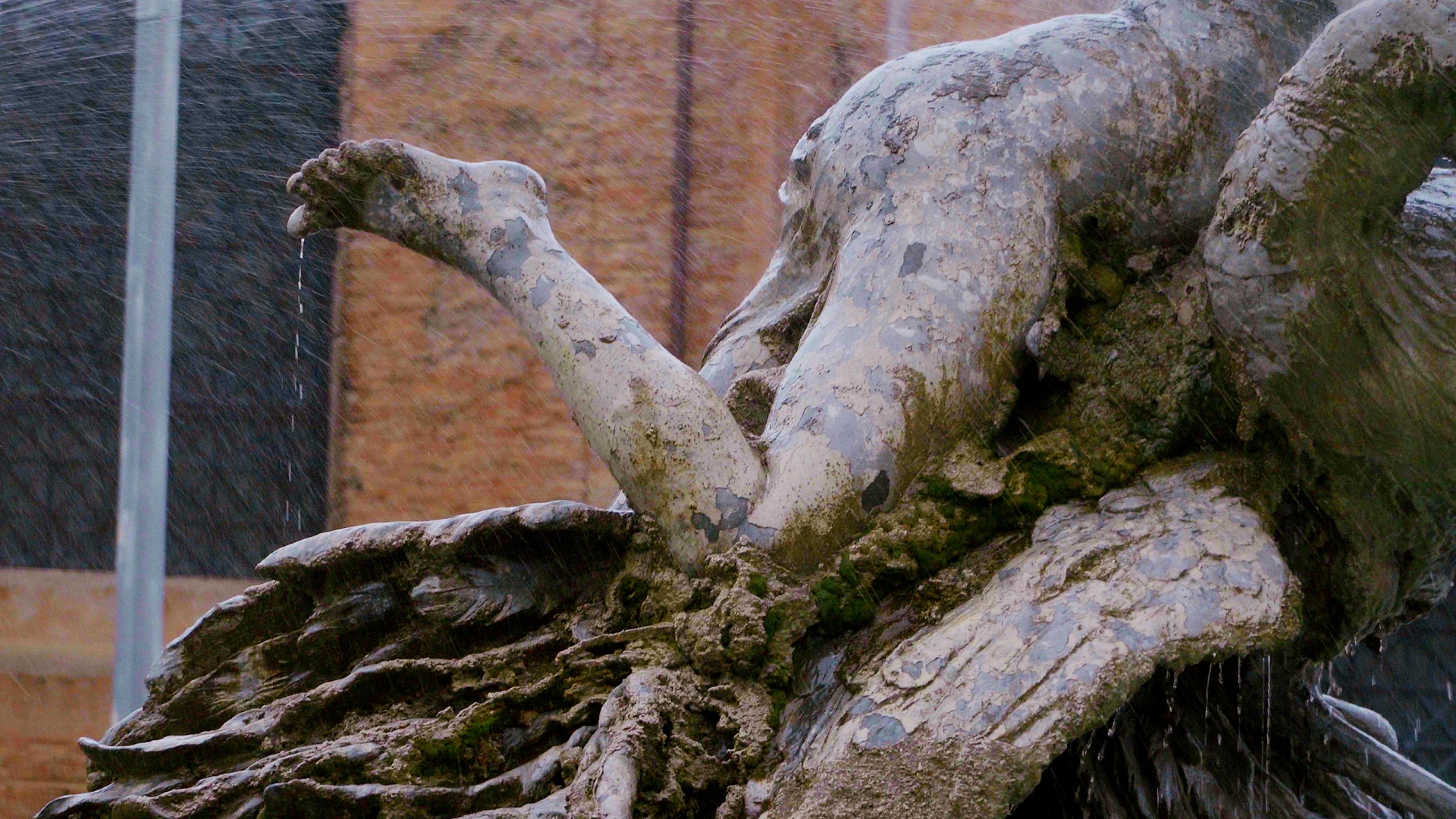 Filmstill, der einen Teil einer Brunndenfigur, den Schenkel einer weiblichen Figur zeigt.