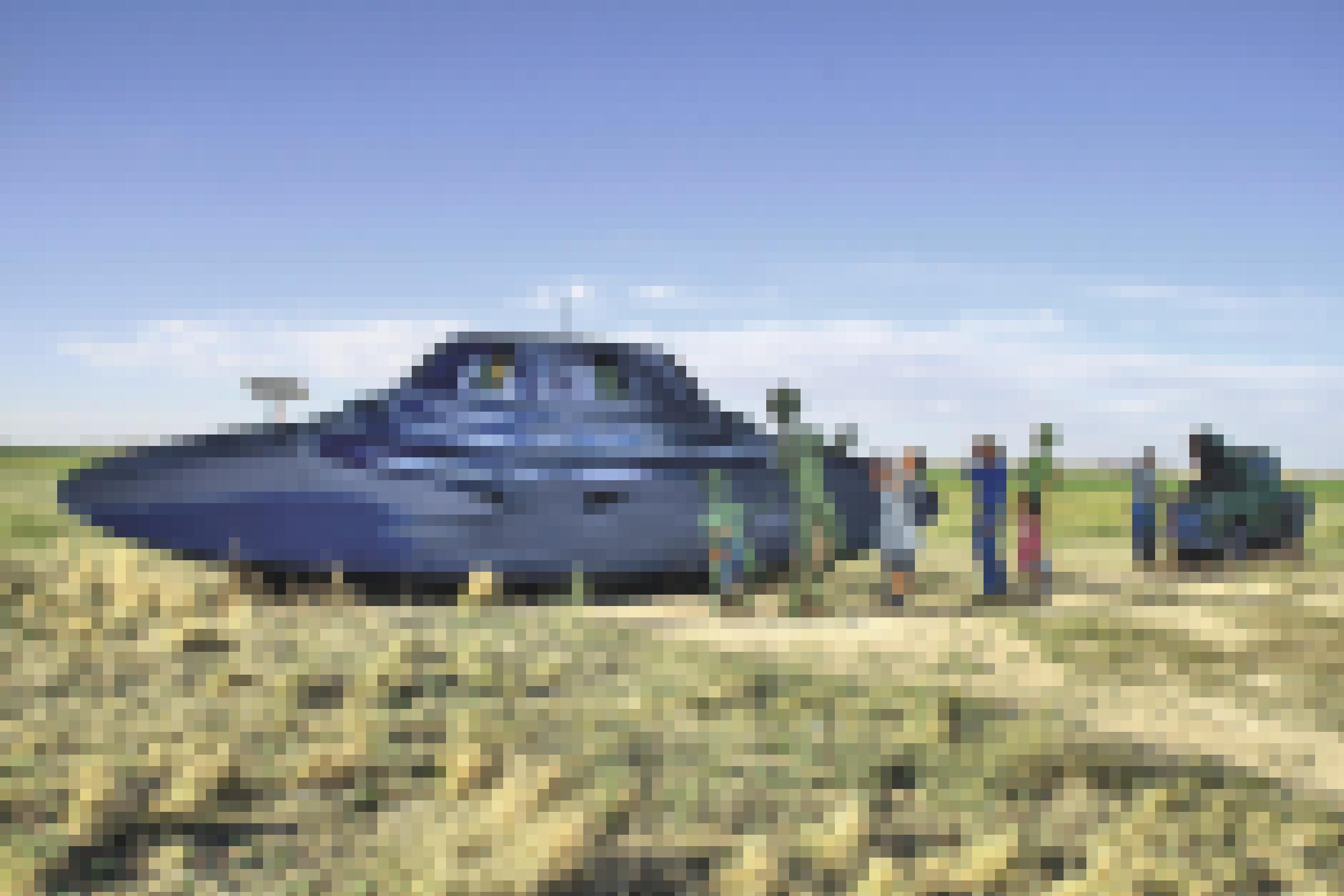 Ein Ufo aus Pappe liegt auf einem Feld. Daneben stehen Pappfiguren, die wie Farmer aussehen und dem Ufo "Starthilfe" geben.