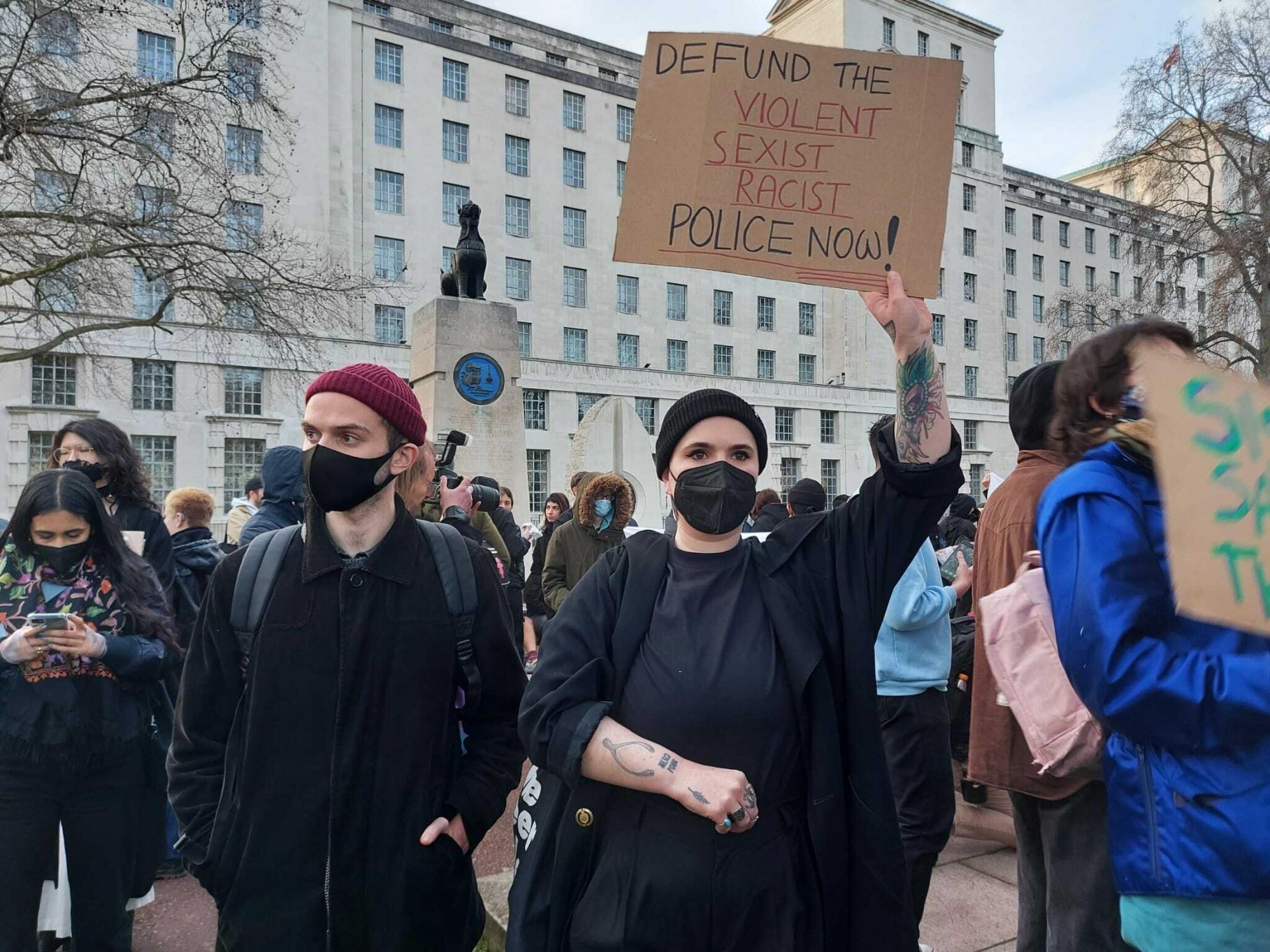 Eine Protestierende hält ein Schild hoch, auf dem steht: Defund the violent and sexist Police now!