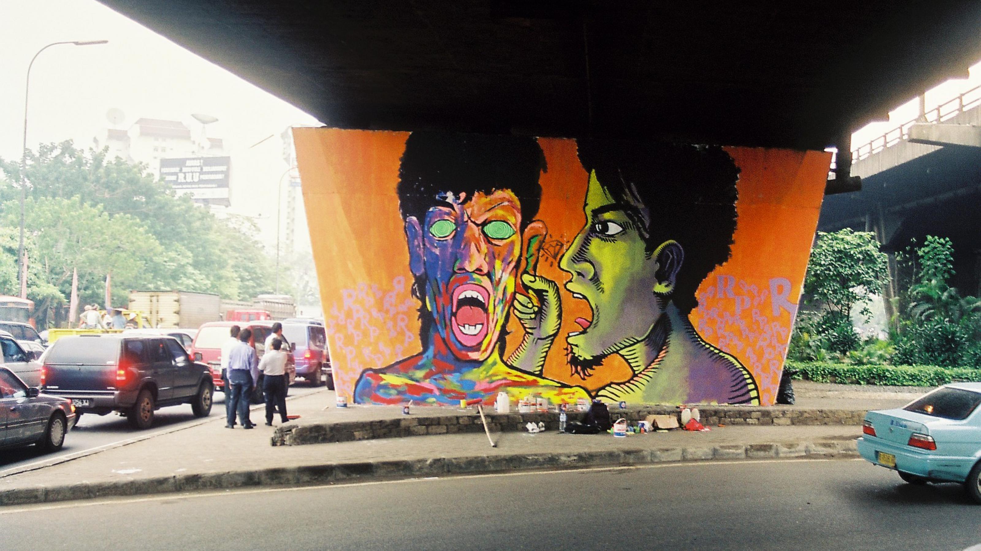 Knalliges Wandbild mit zwei großen Köpfen an einer Betonwand unter einer Autobahnunterführung in Jakarta 2001