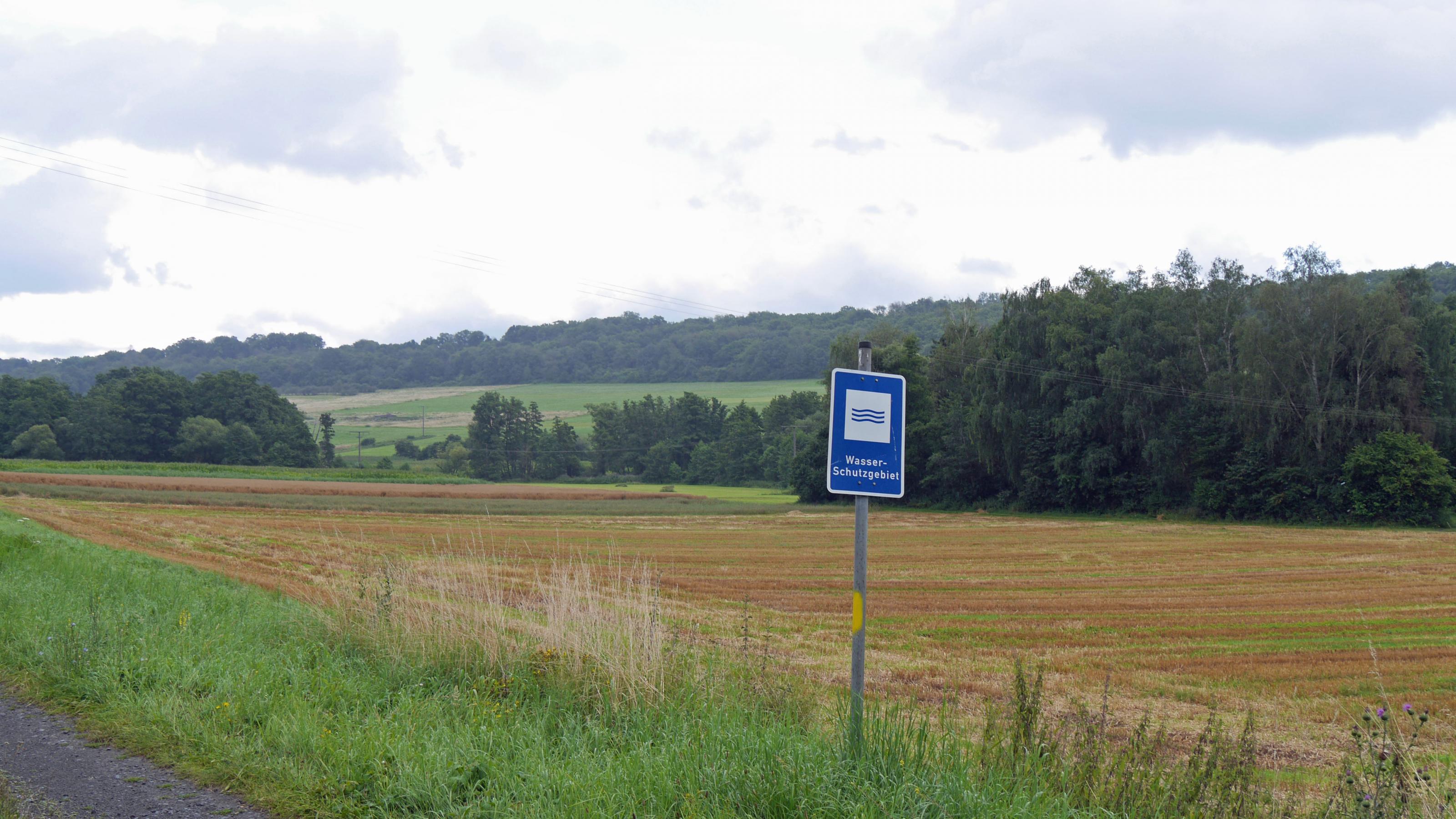 Schild Wasserschutzgebiet vor einem abgeernteten Getreidefeld und einem Waldsaum