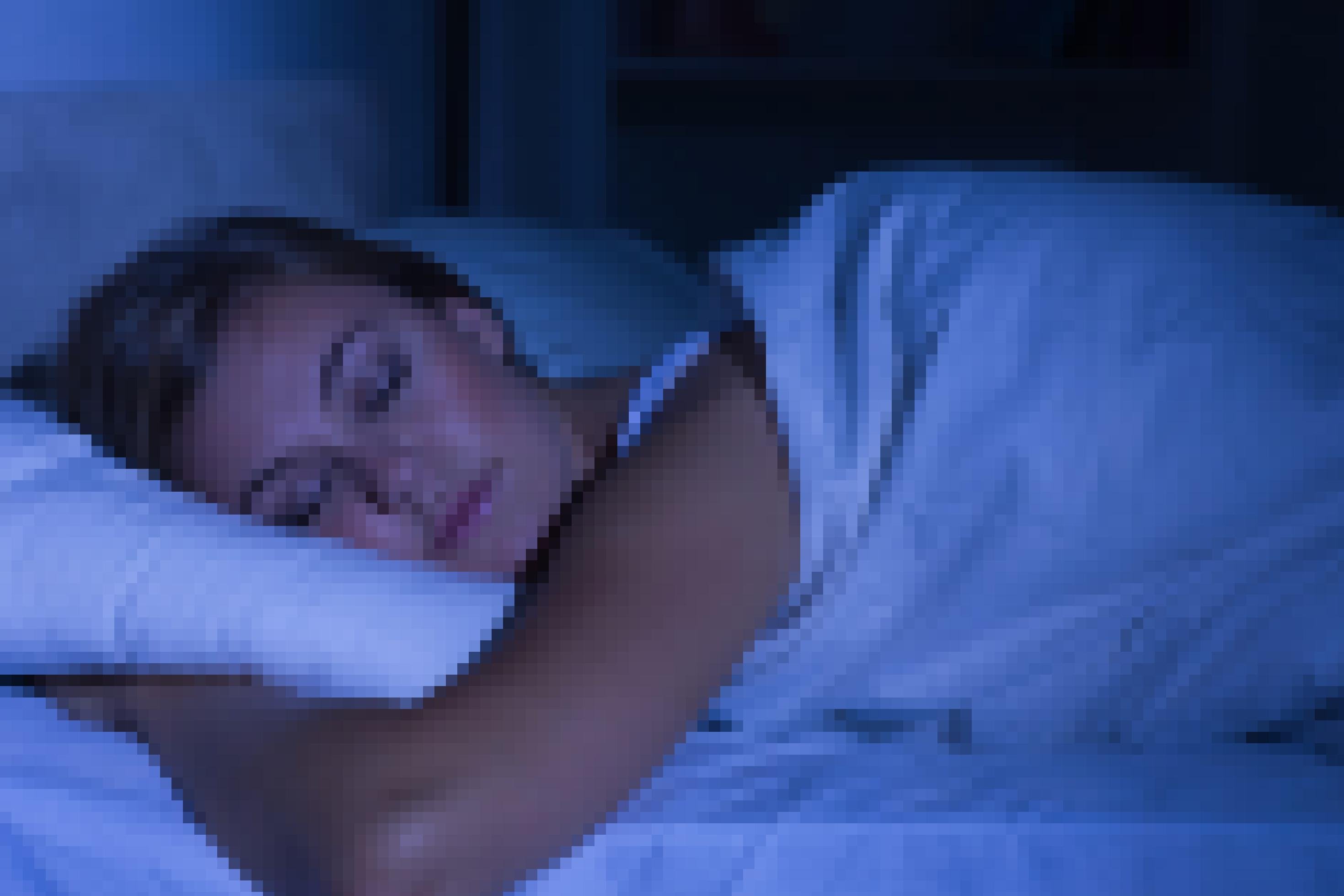 Das Foto zeigt Kopf, Arm und Schulter einer jungen Frau, die eingekuschelt in ihre Bettdecke friedlich schlummert. Die Szene ist in blaues, dämmrig wirkendes Licht getaucht.