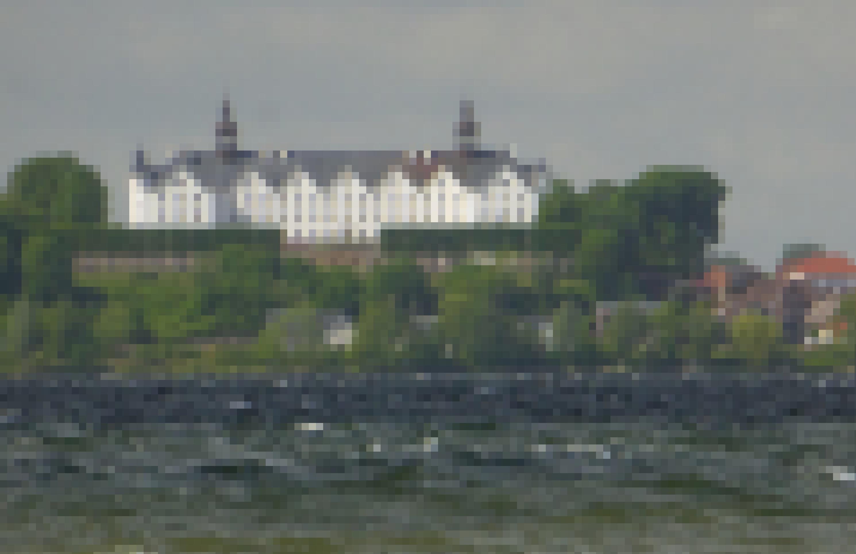Die weiße Fassade des Plöner Schlosses glänzt zwischen dessen grauem Dach und dem grauen, aufgewühlten See davor.