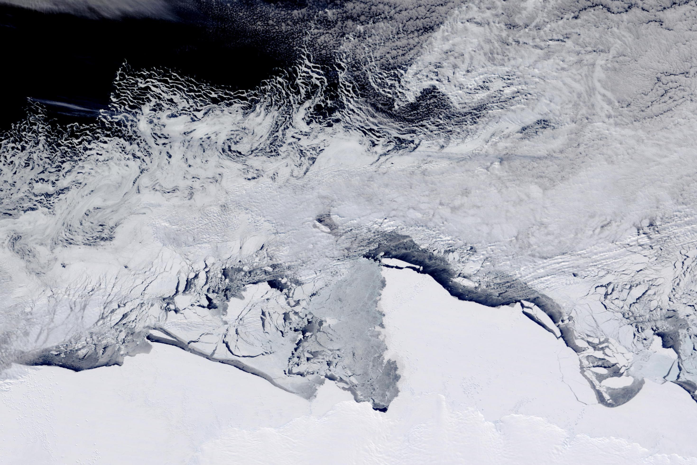 Eine Landschaft aus Satelliten-Perspektive: eine eisbedeckte Küste, eine Zone mit Eisbergen, dunkel erscheinendes Wasser