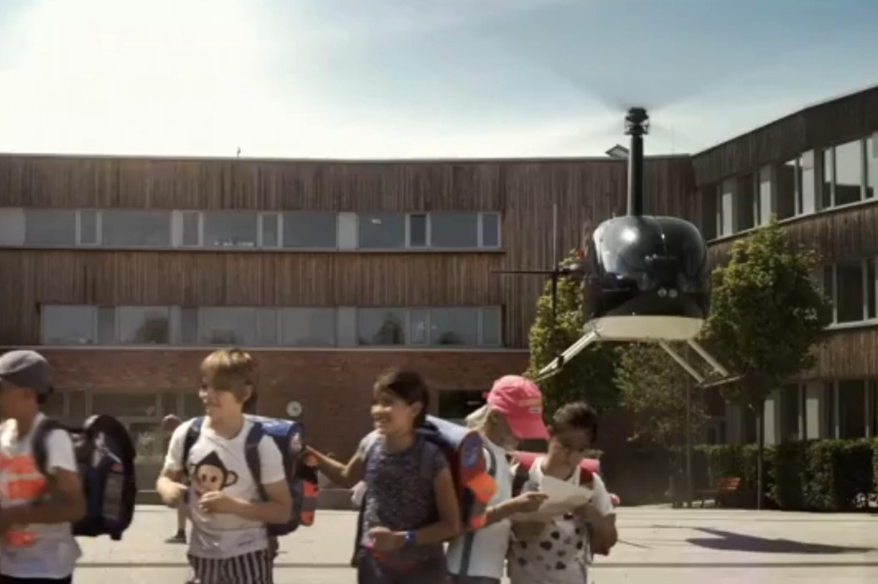 Ein Hubschrauber startet vom Schulhof, gerade hat ein Vater sein Kinder zur Schule gebracht. Die Szene stammt aus einem Film der Stadt Frankfurt/Main zum Thema Elterntaxis.