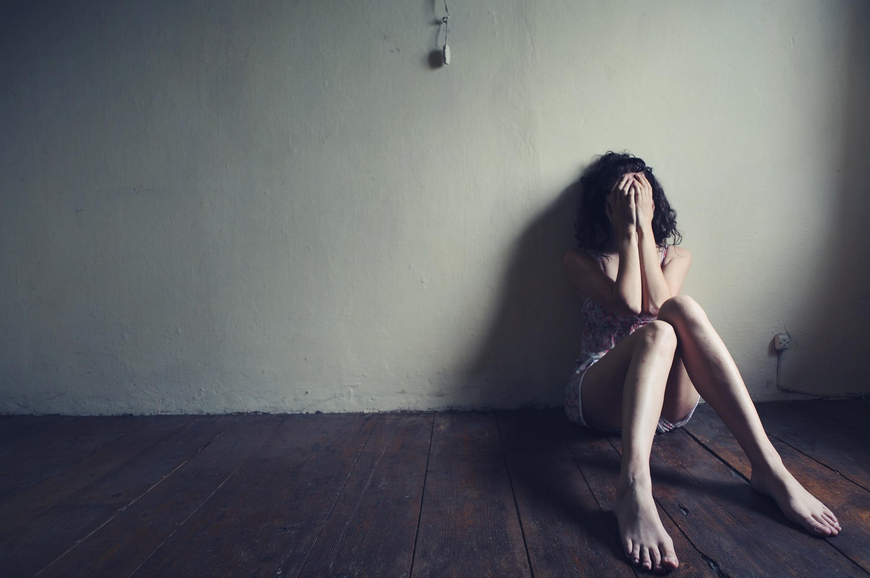 Eine traurige Frau sitzt alleine in einem leeren Zimmer.