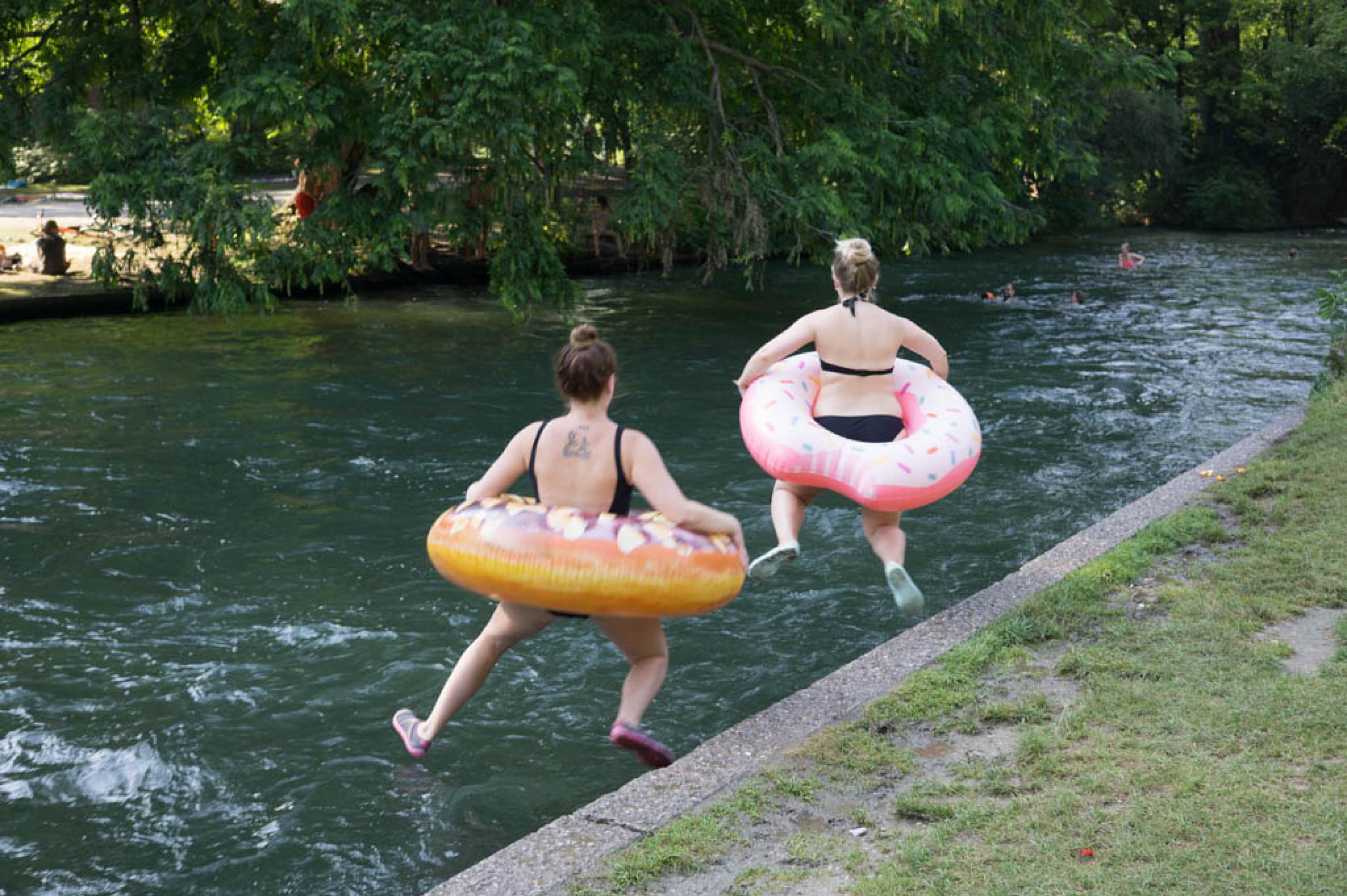 Zwei Frauen mit Schwimmreifen springen in Kanal.