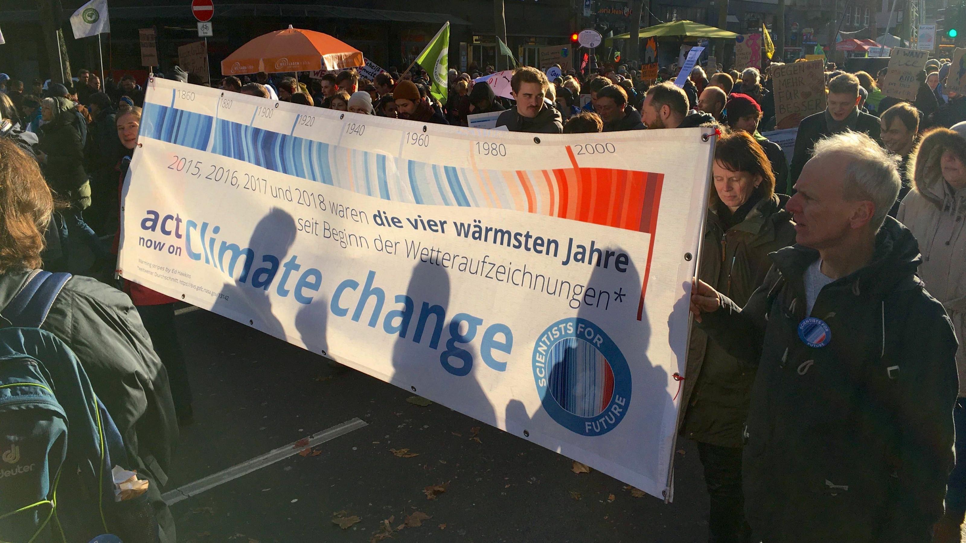 Szene vom Klimastreik 2019 in Köln. Aktivst:innen von Scientists for Future tragen ein Banner mit den Warming Stripes und dem Hinweis, dass die Jahre 2015 bis 2018 jeweils Temperaturrekorde erreicht haben.