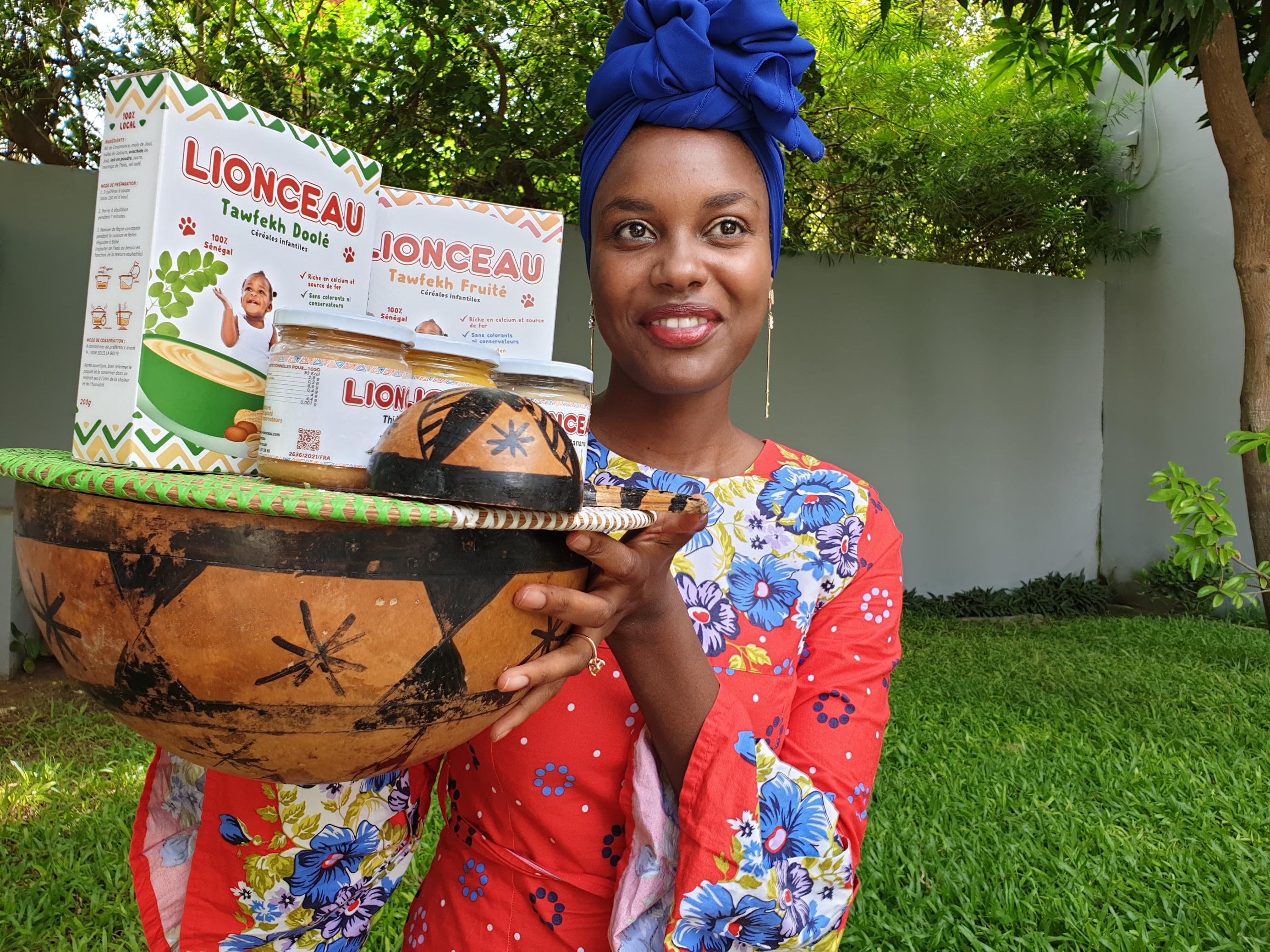 Siny Samba, Mitbegründerin des senegalesischen Babynahrungsherstellers Le Lionceau, steht in ihrem Garten und trägt eine Kalebasse mit verschiedenen Pürees, die ihr Unternehmen herstellt.