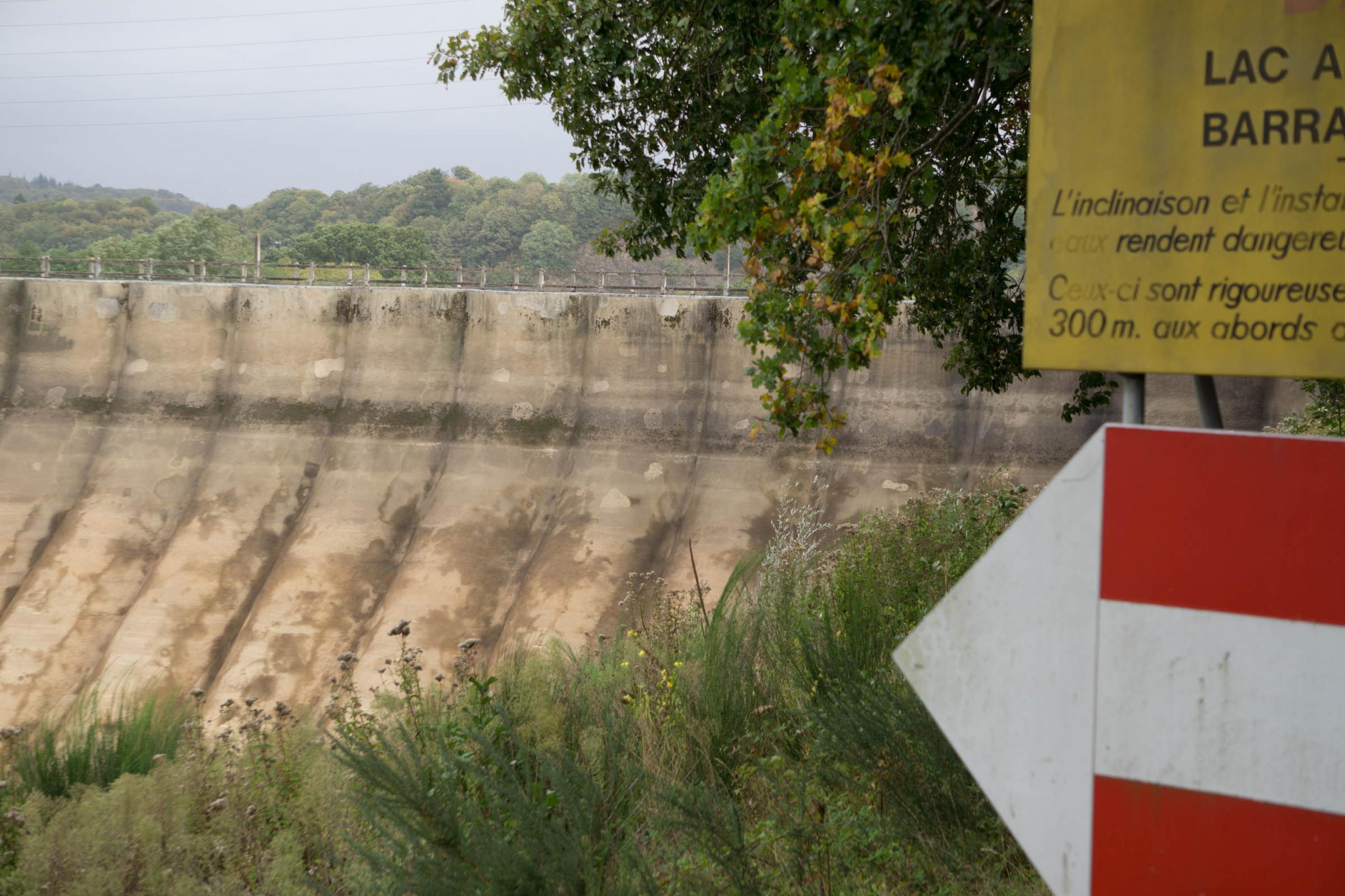 Ein großer alter Staudamm, rechts davon Hinweisschilder.