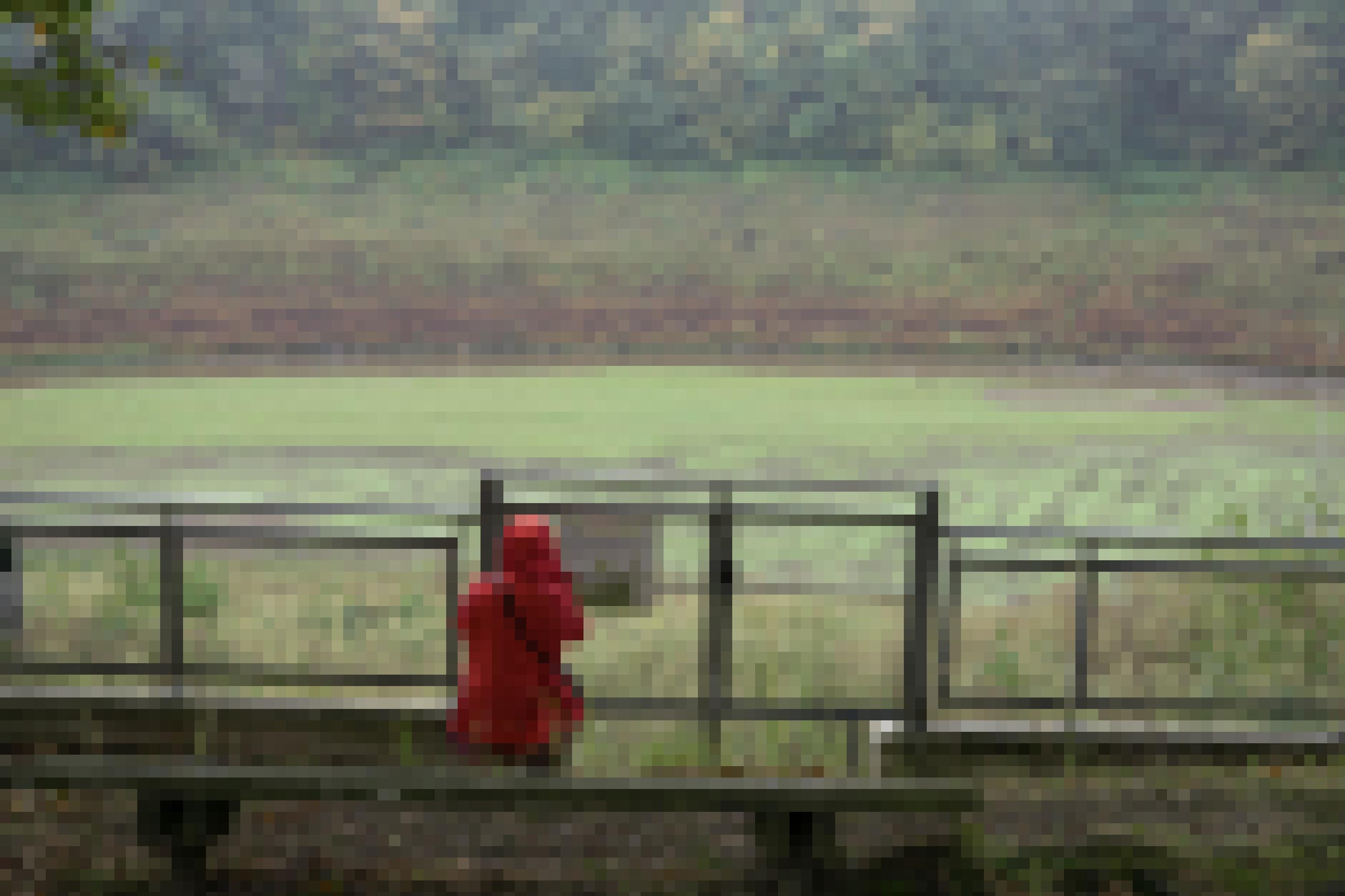 Zaun vor trocken gelegtem Stausee, davor eine Person mit roter Regenjacke