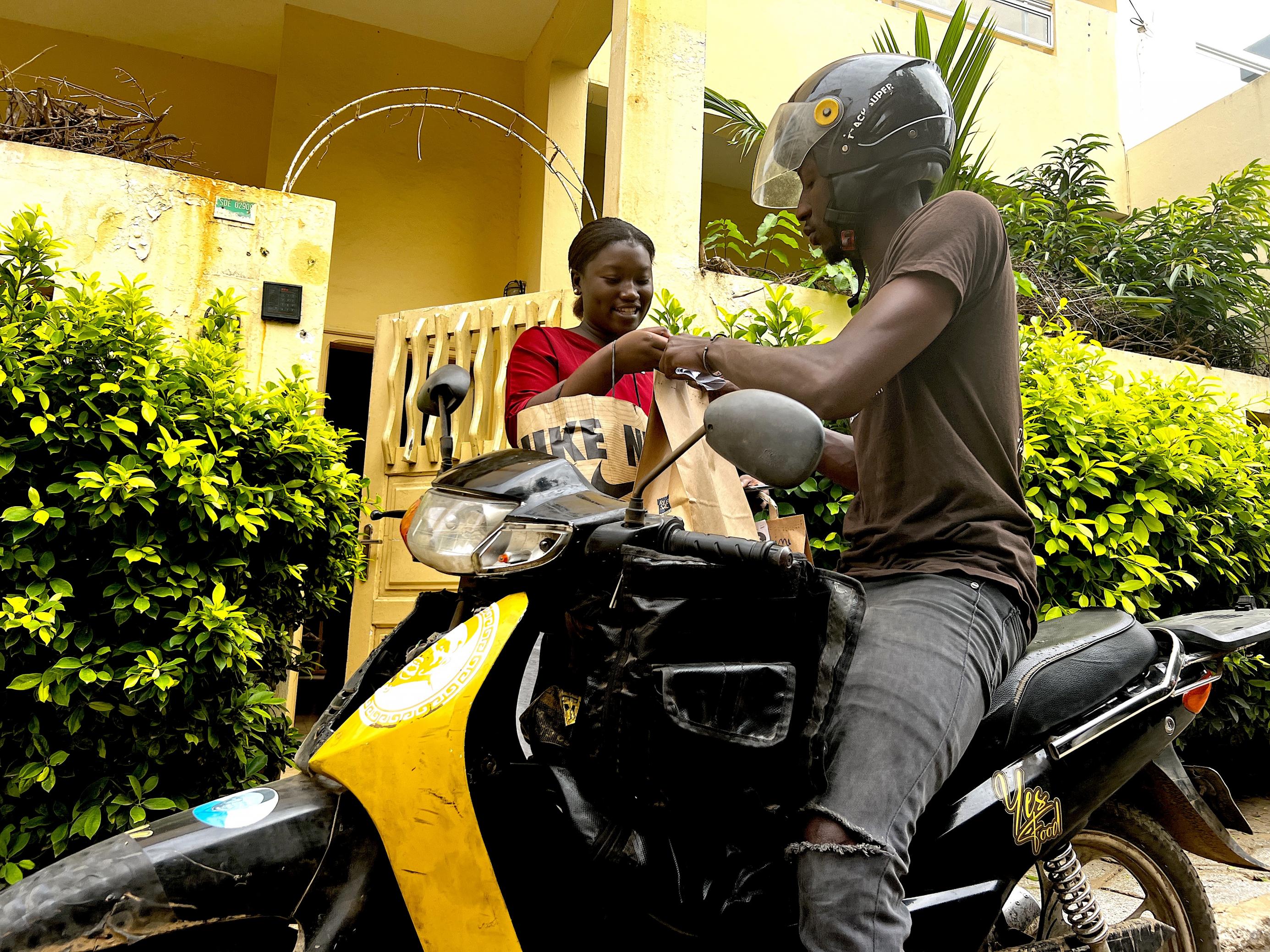 Dakar, Senegal: Aissatou Ngom tauscht Pakete mit einem Auslieferungsfahrer aus, er gibt Altgläser zurück, sie übergibt Babynahrungspüreegläser zur Auslieferung an Kunden.