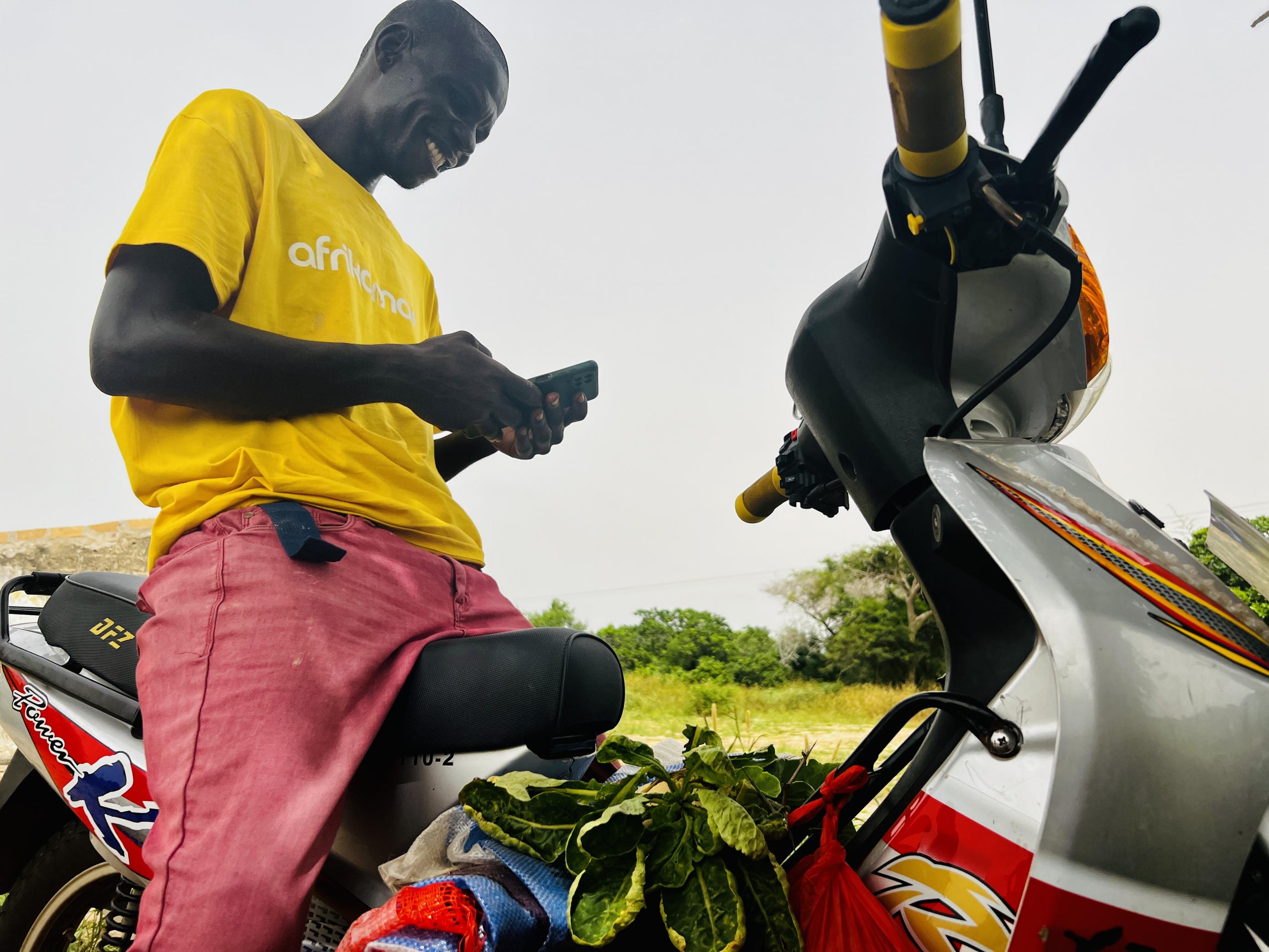 Ein Mann sitzt an seinem Telefon, lächelt und überprüft seine Nachrichten in Mbour, Senegal.